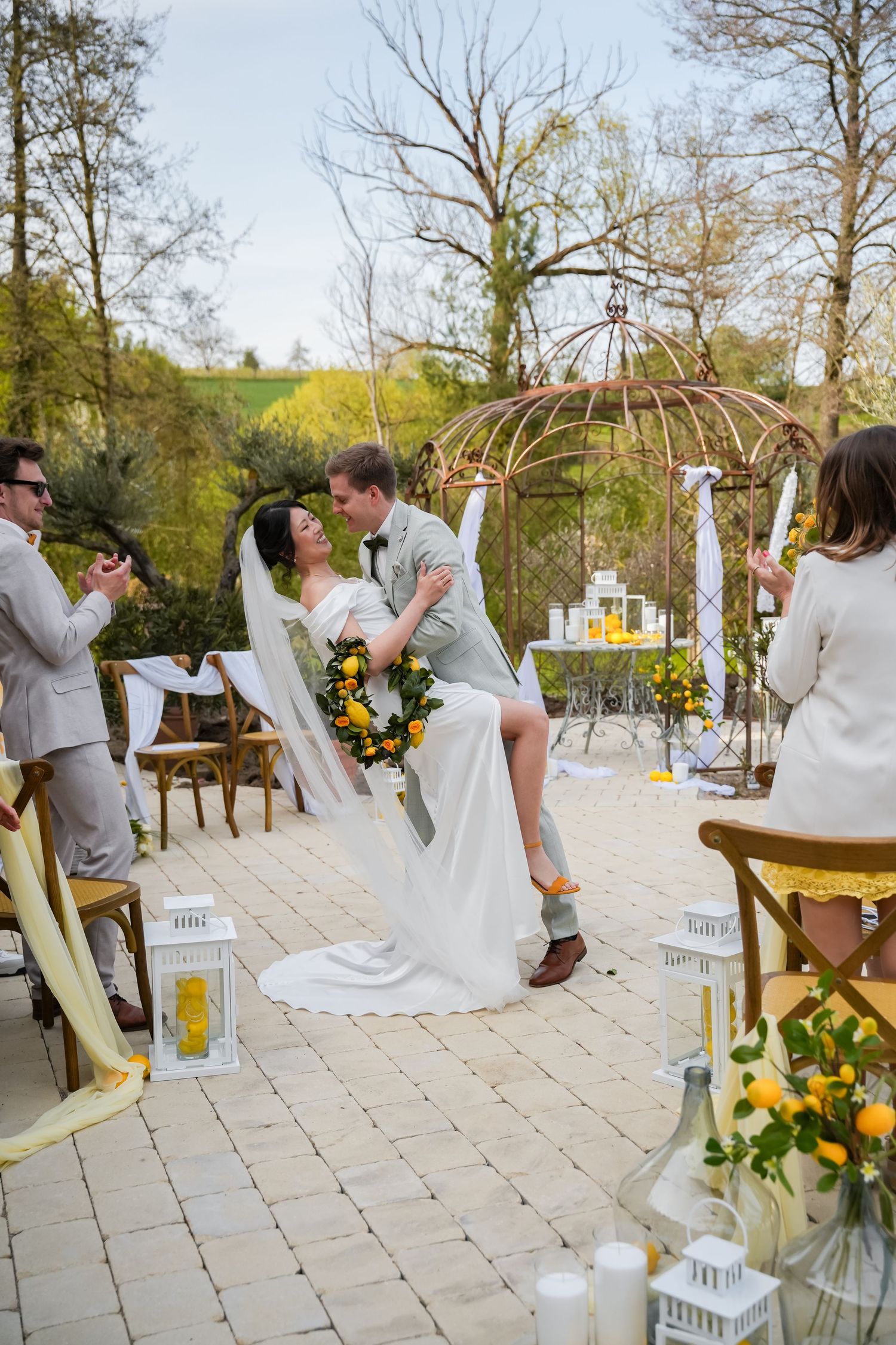 Bride and groom share a romantic dip kiss at outdoor wedding ceremony with yellow floral decor and gazebo.
