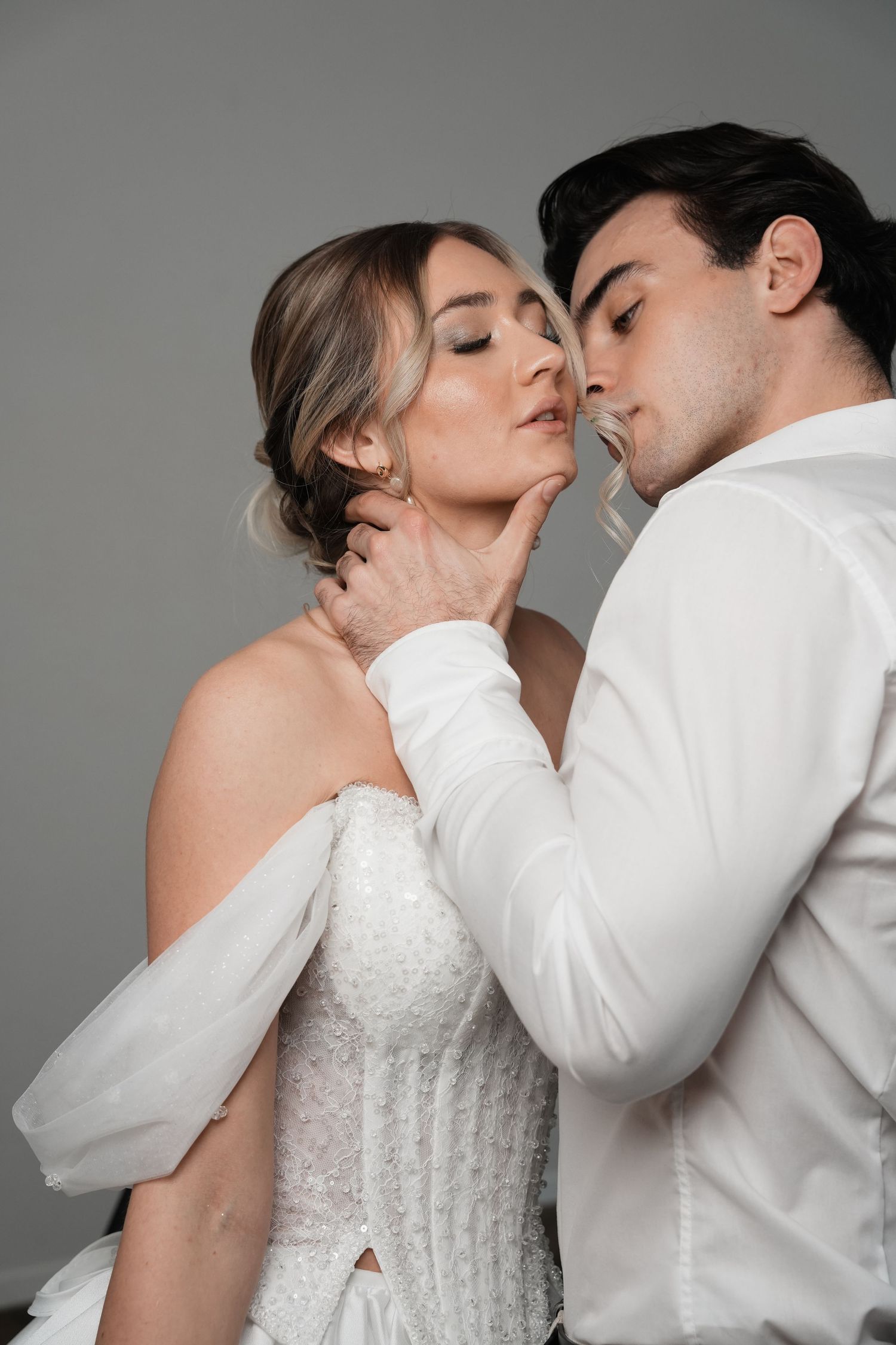 Romantic couple in white wedding attire sharing an intimate moment, groom gently holding bride's face.