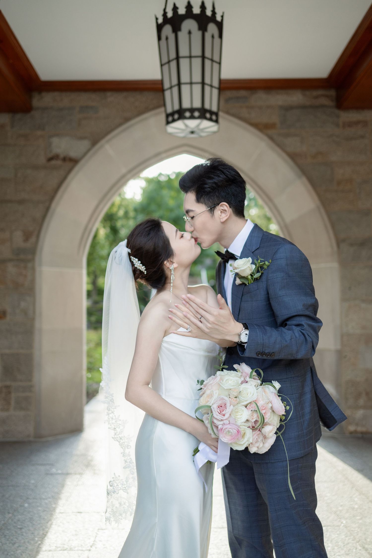Romantic wedding moment captured under a stone archway with hanging lantern.