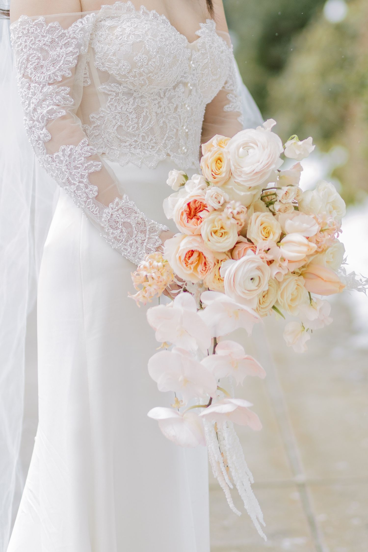 Elegant wedding dress detail with lace bodice and soft peach and cream floral bouquet.