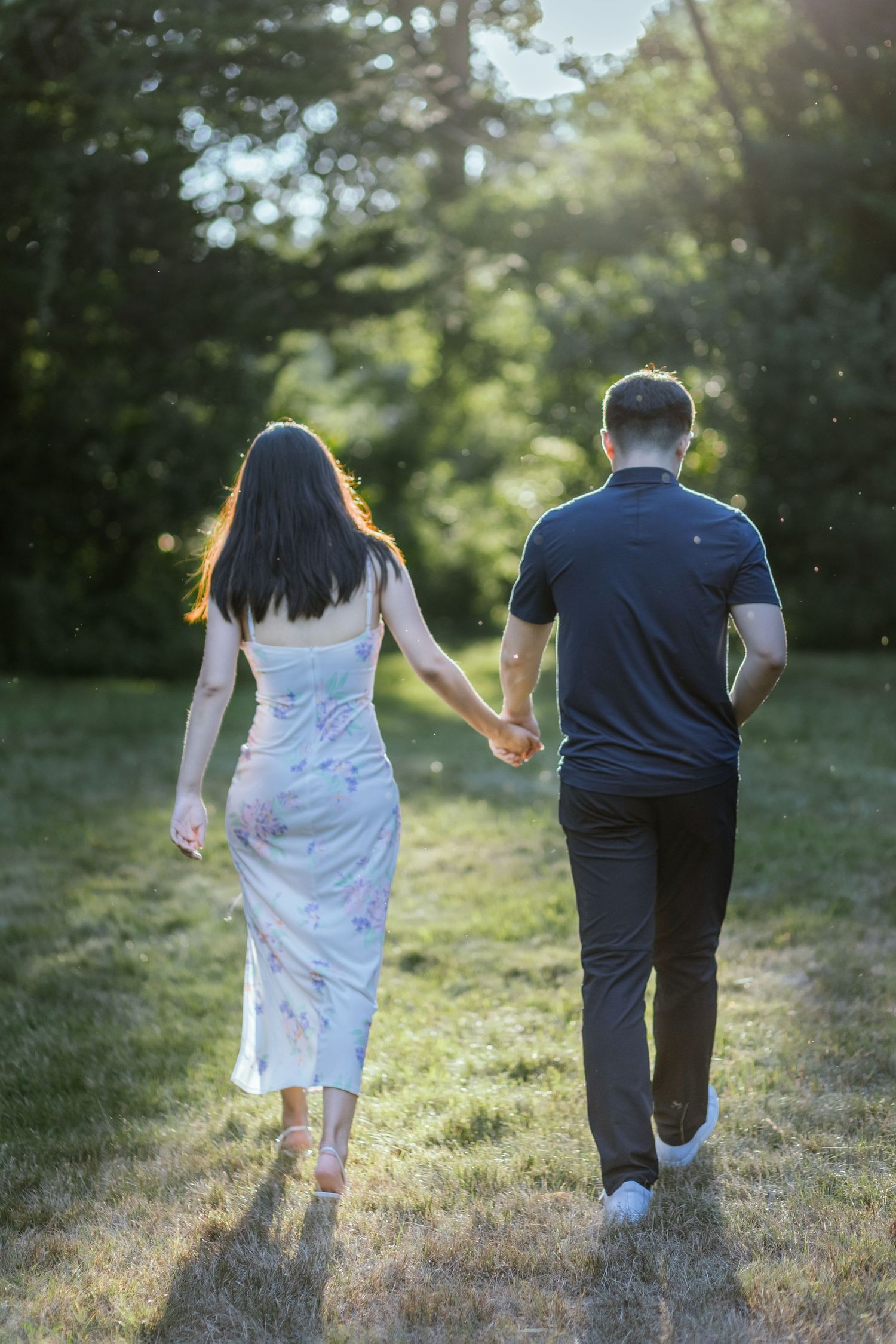 Couple running playfully through sunlit grassy field in formalwear.