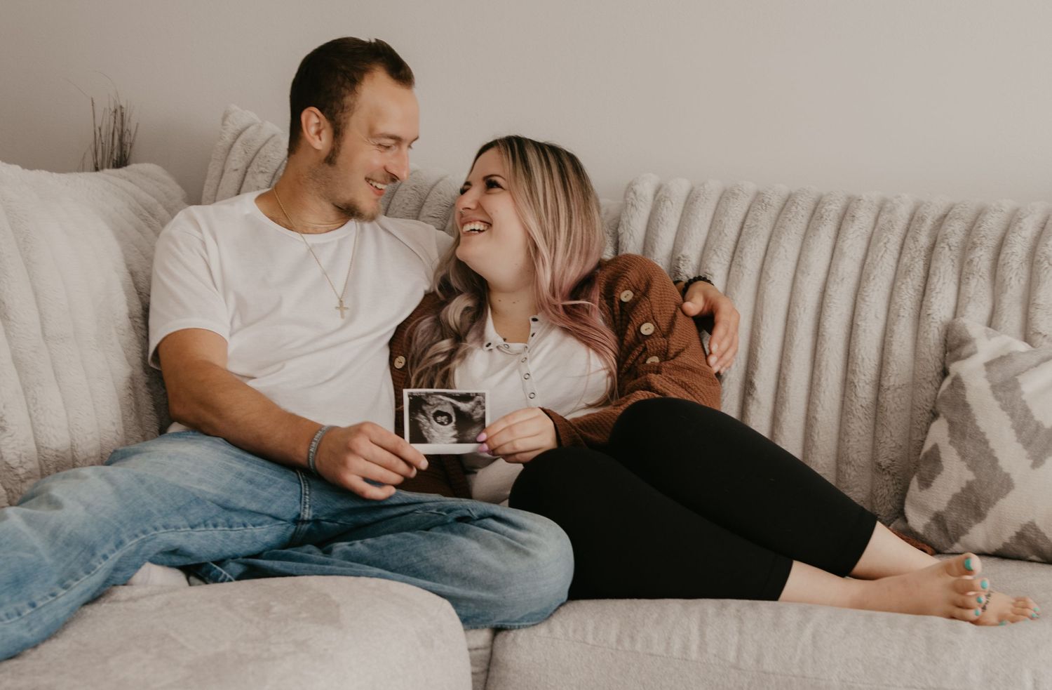 Happy couple sitting on a couch together holding an ultrasound photo announcing pregnancy.
