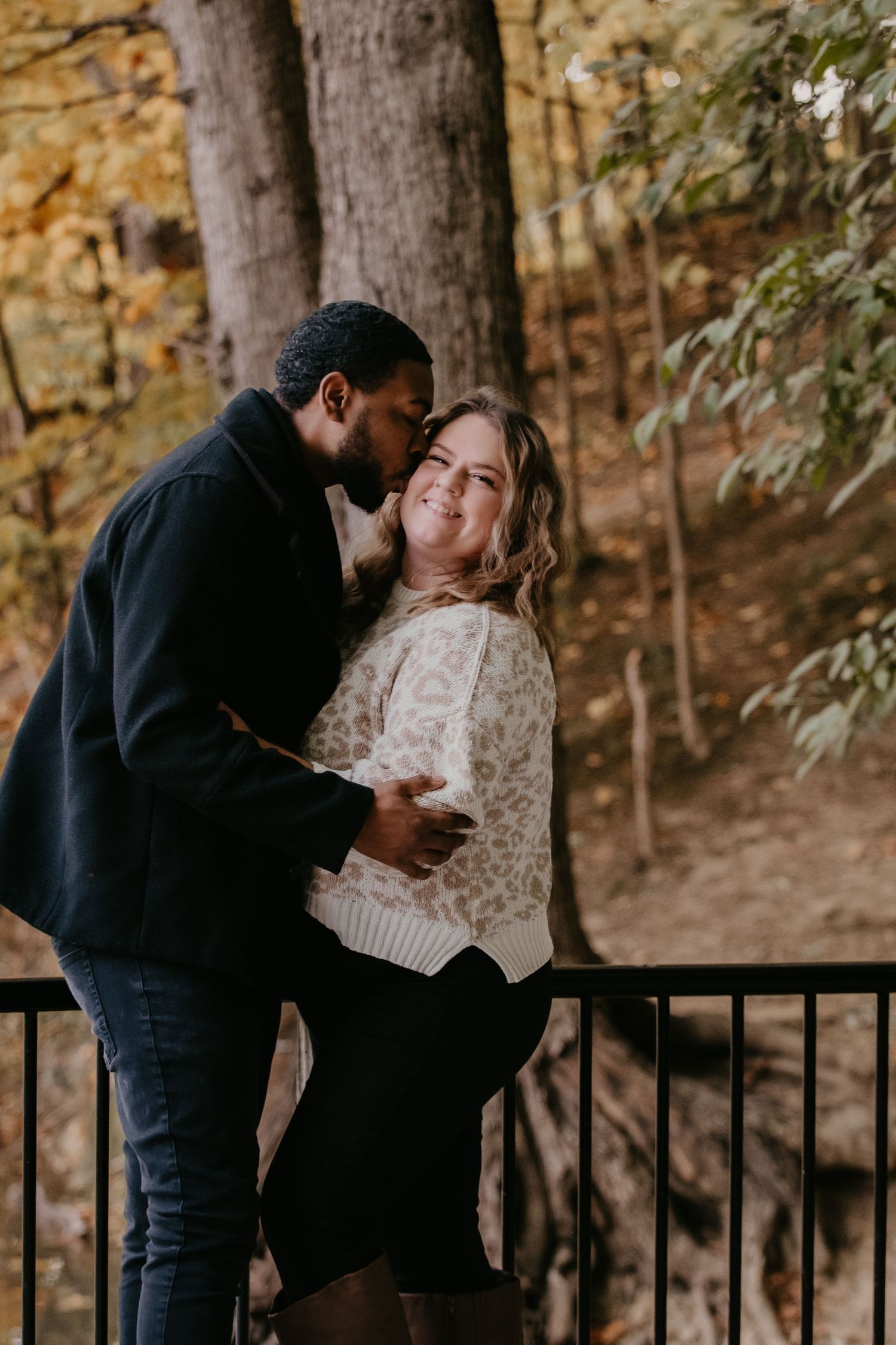 Couple embracing romantically on wooden bridge surrounded by colorful autumn foliage.