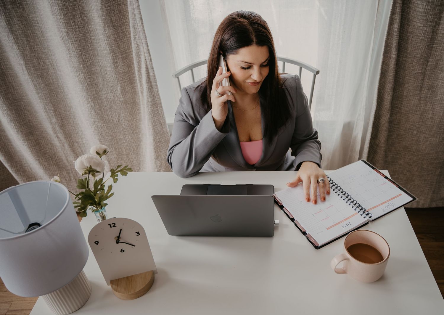 Professional woman on phone call while working on laptop at home office desk.