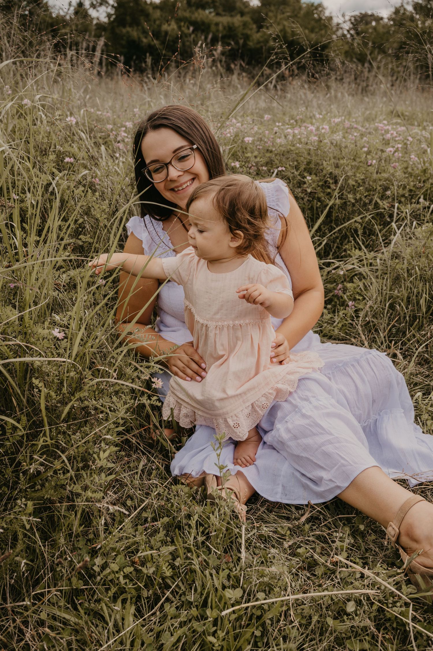 Smiling mother wearing glasses sitting in a wildflower field with her baby girl.