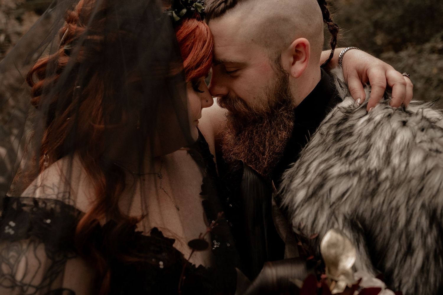 Couple in dark romantic attire sharing an intimate moment outdoors in a gothic style.