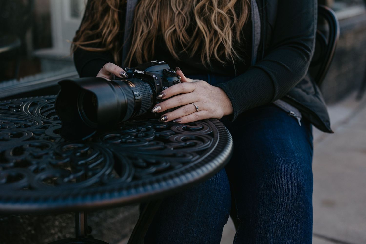 Woman with wavy hair holding a professional DSLR camera with zoom lens resting on ornate black iron table.