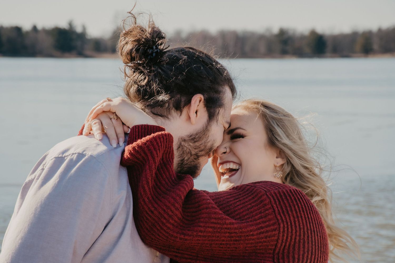 Joyful couple laughing and embracing outdoors near a lake in autumn.
