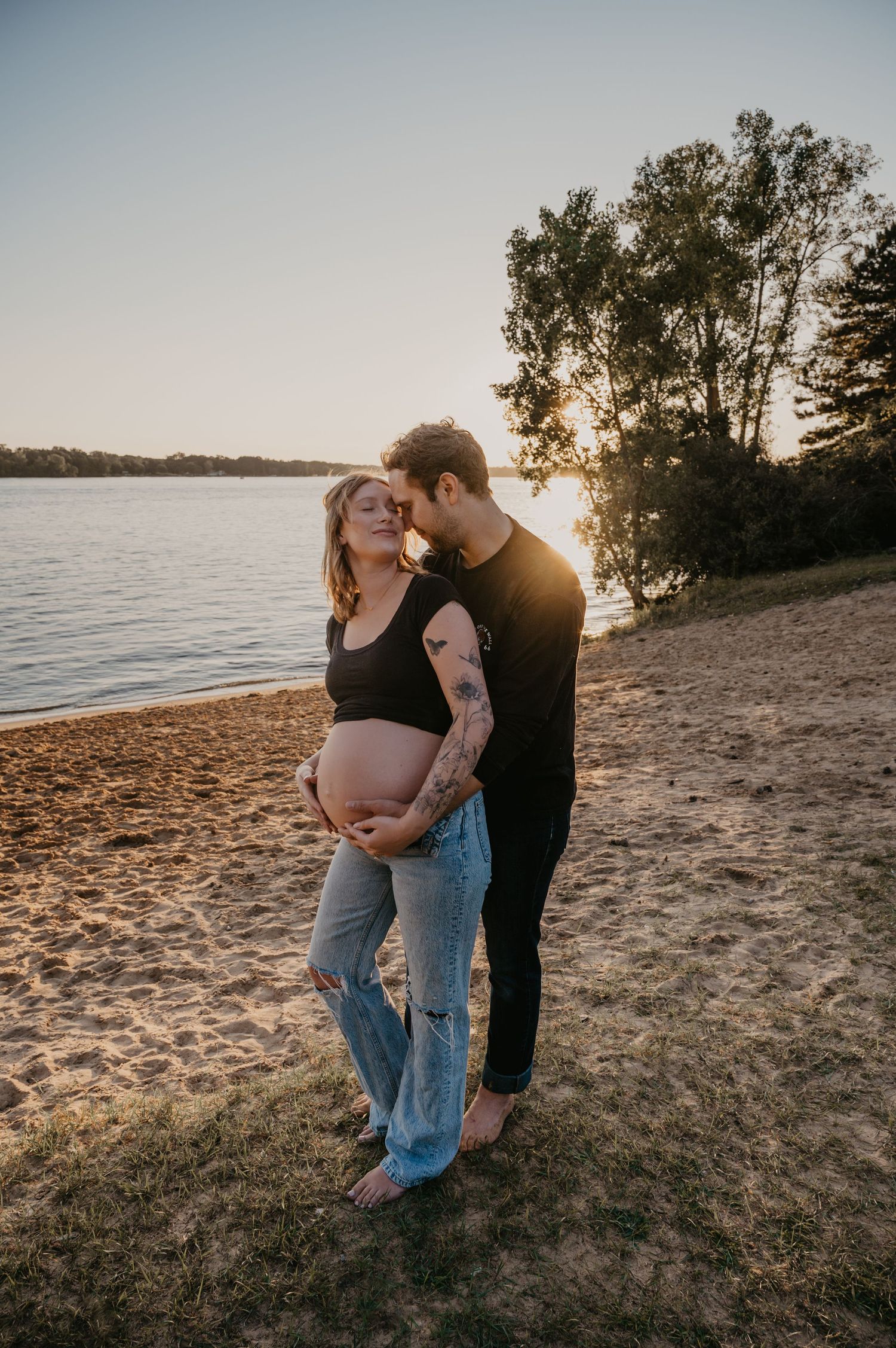 Expecting couple embracing on a sandy beach at golden hour during a maternity photoshoot.