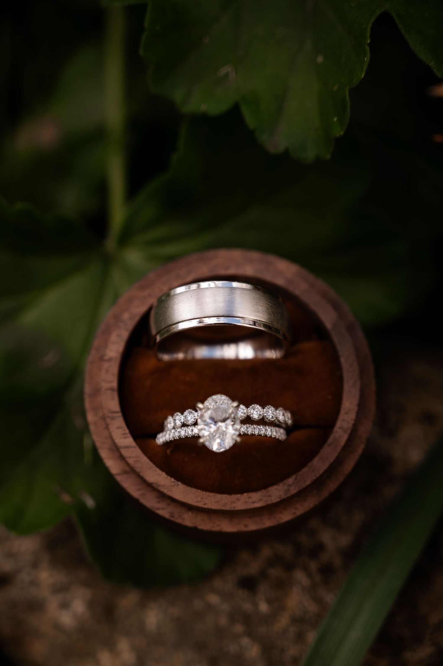 Oval diamond engagement ring and wedding band set in a wooden ring box with greenery.