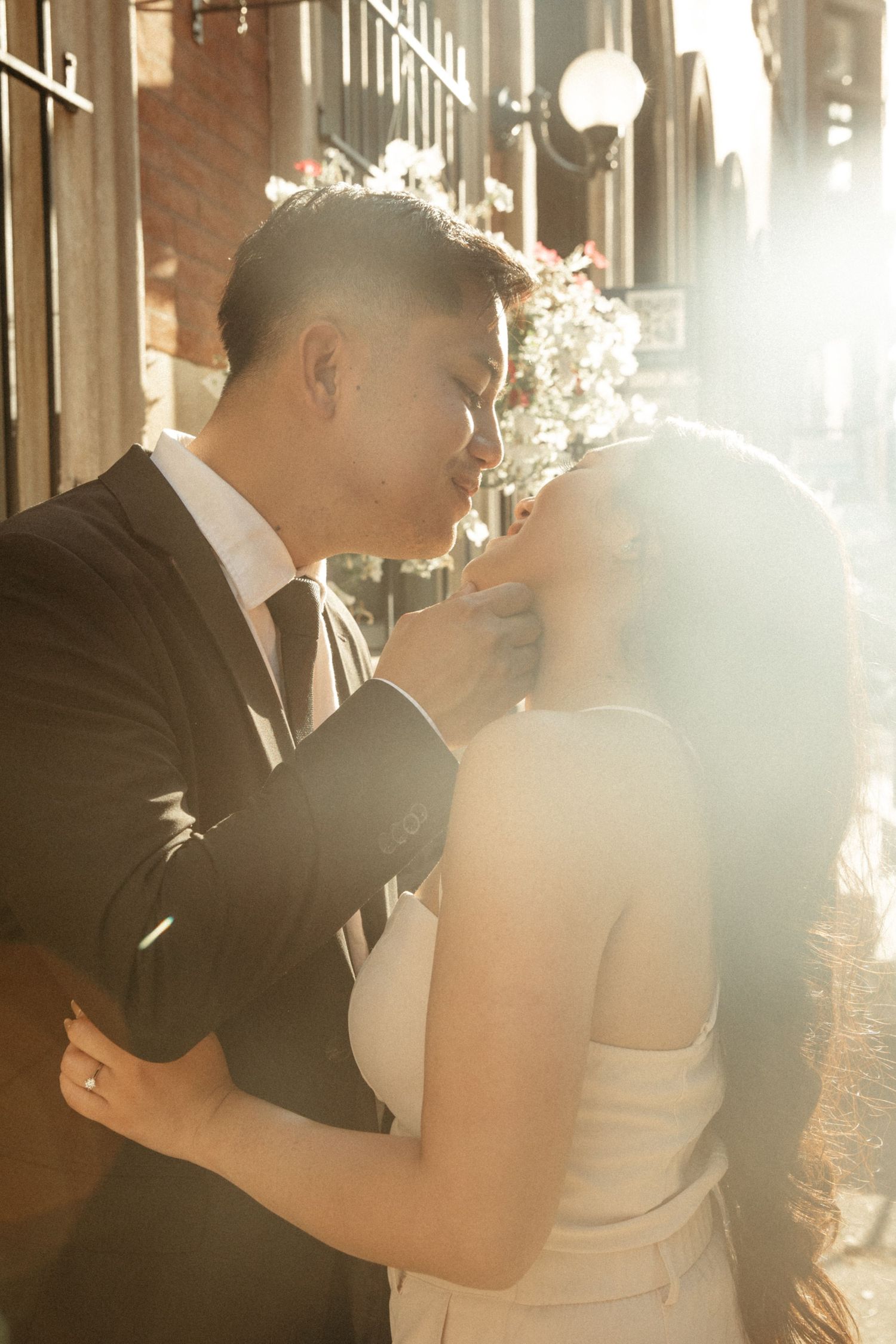 A backlit wedding couple embraces in a romantic moment as sunlight streams through creating a dreamy atmosphere.