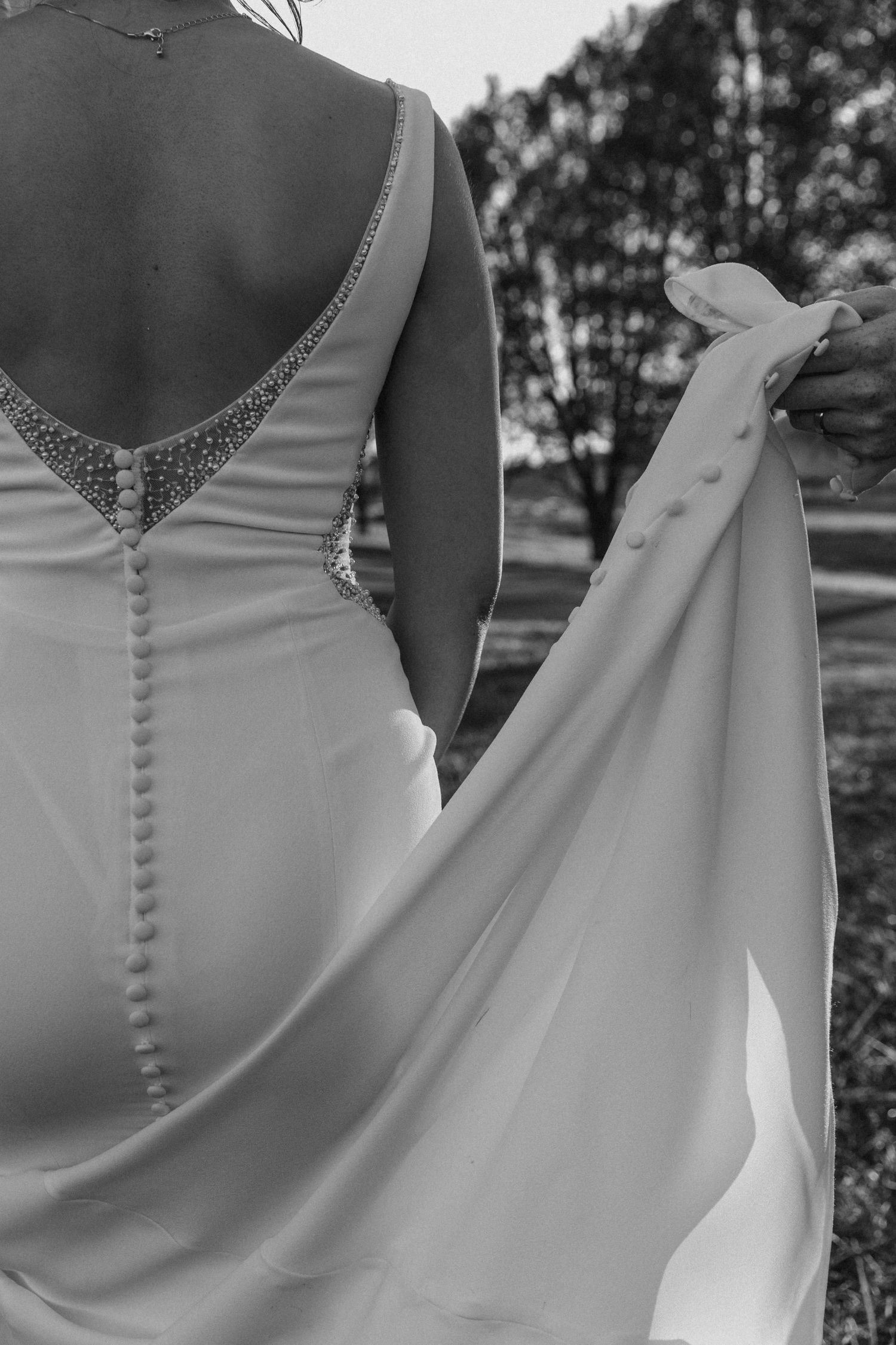 Close-up black and white photo of a wedding dress back with delicate buttons and beaded V-neck detail.
