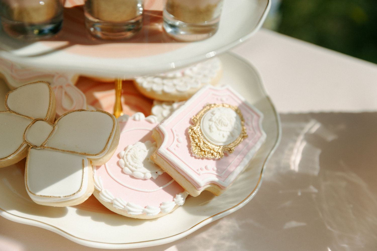 Elegant pink and white frosted cookies with ornate decorative details arranged on a white plate in sunlight.