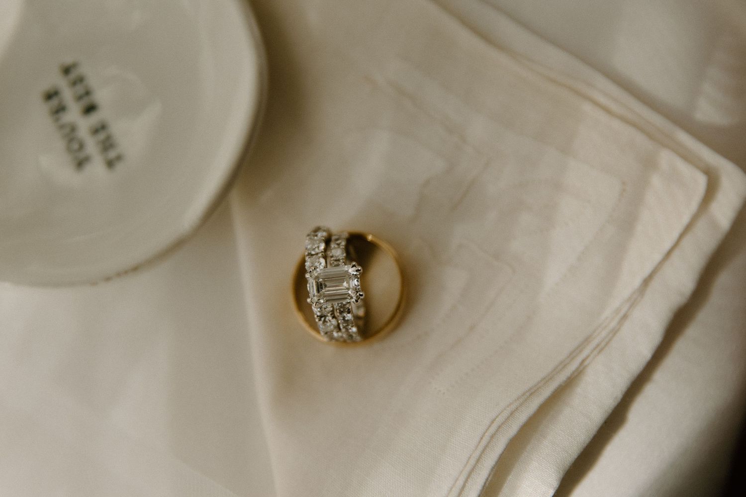 Gold wedding rings with diamonds resting on white fabric near a ceramic plate.