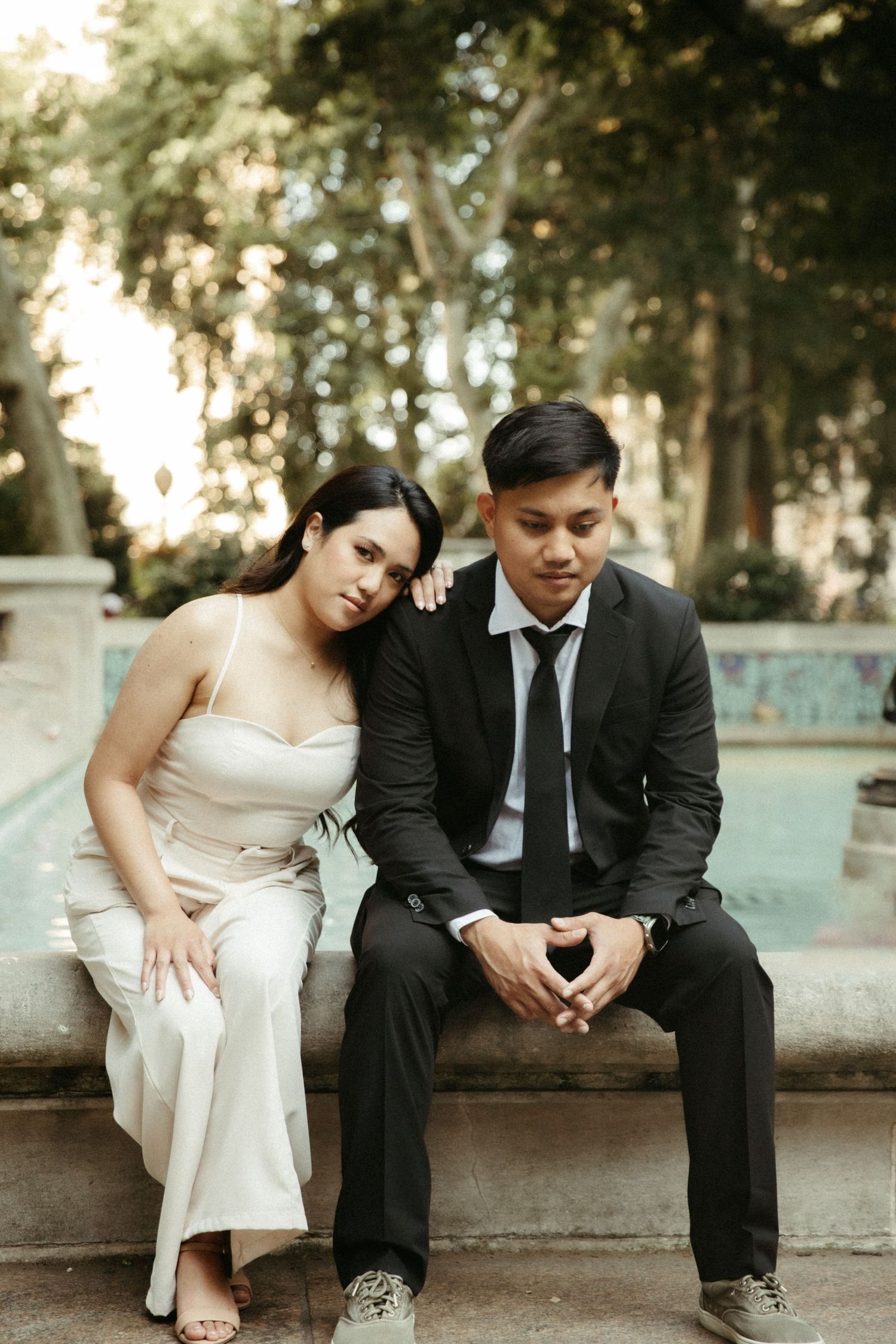 A couple in wedding attire sits together on stone steps in a romantic outdoor garden setting.