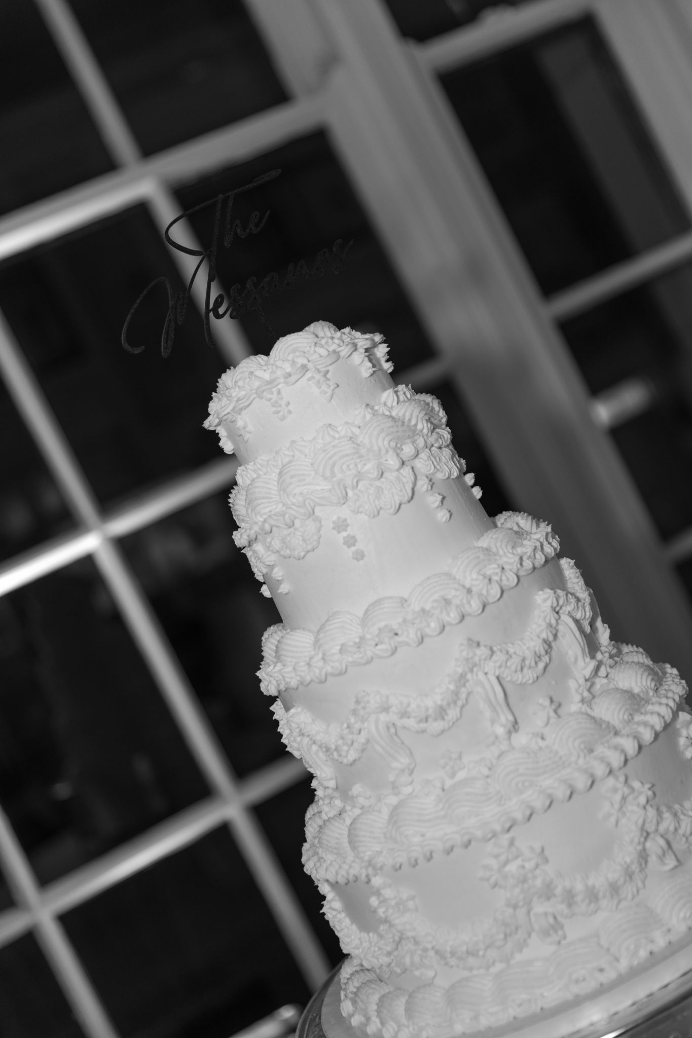 An elegant white tiered wedding cake with intricate piped details and lace-like decorations in black and white photography.