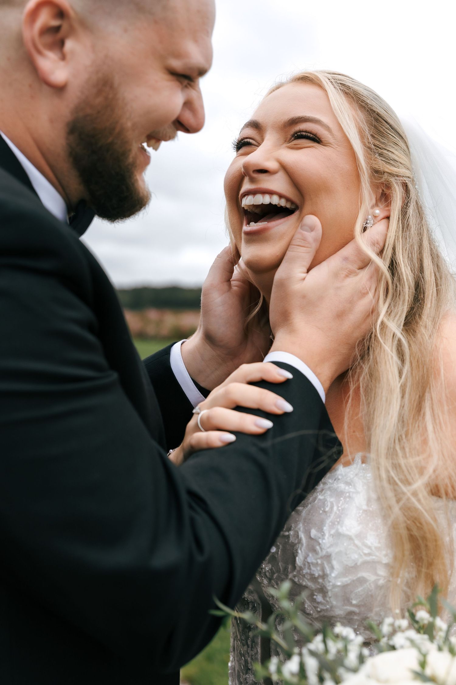A joyful wedding couple shares an intimate candid moment outdoors with genuine laughter and emotion.