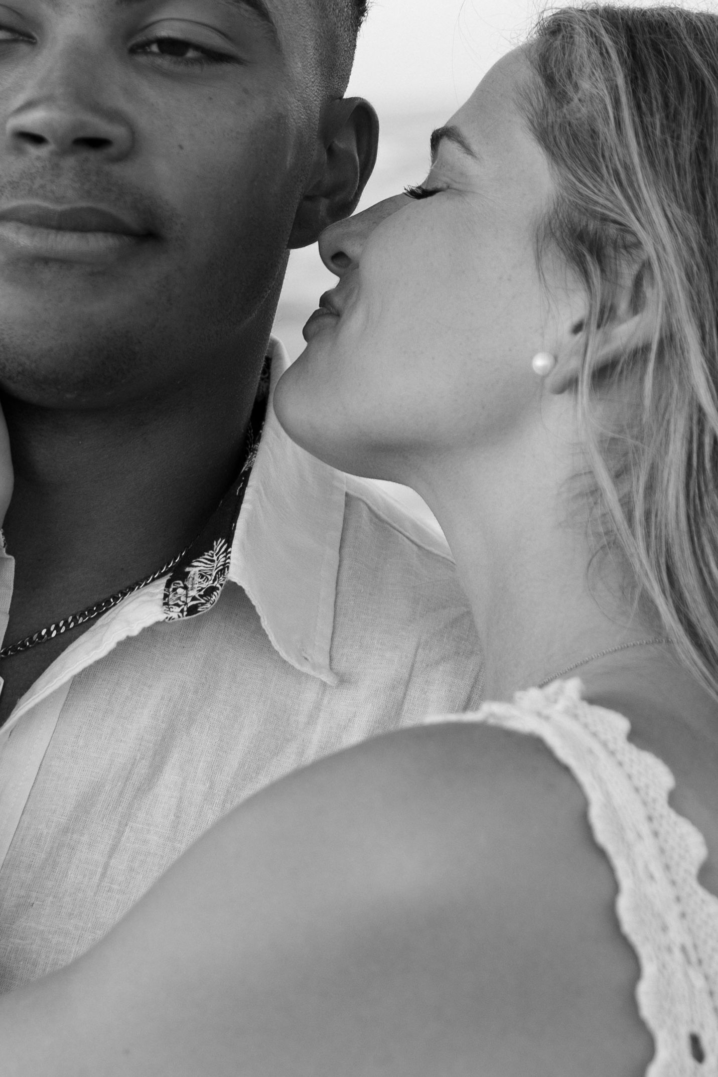 Intimate black and white portrait showing a couple in a tender moment, with one person wearing white lace.