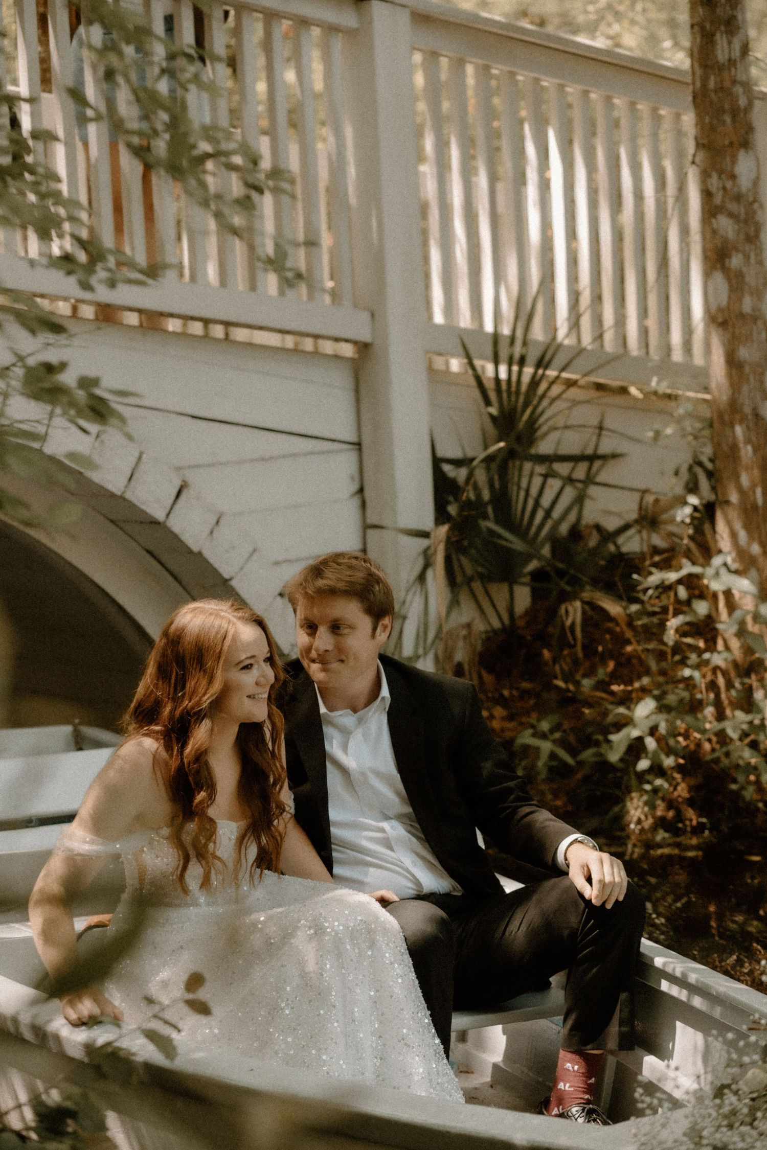 Couple sits intimately on white porch stairs with the bride in a sparkly gown and groom in dark suit for wedding photos.