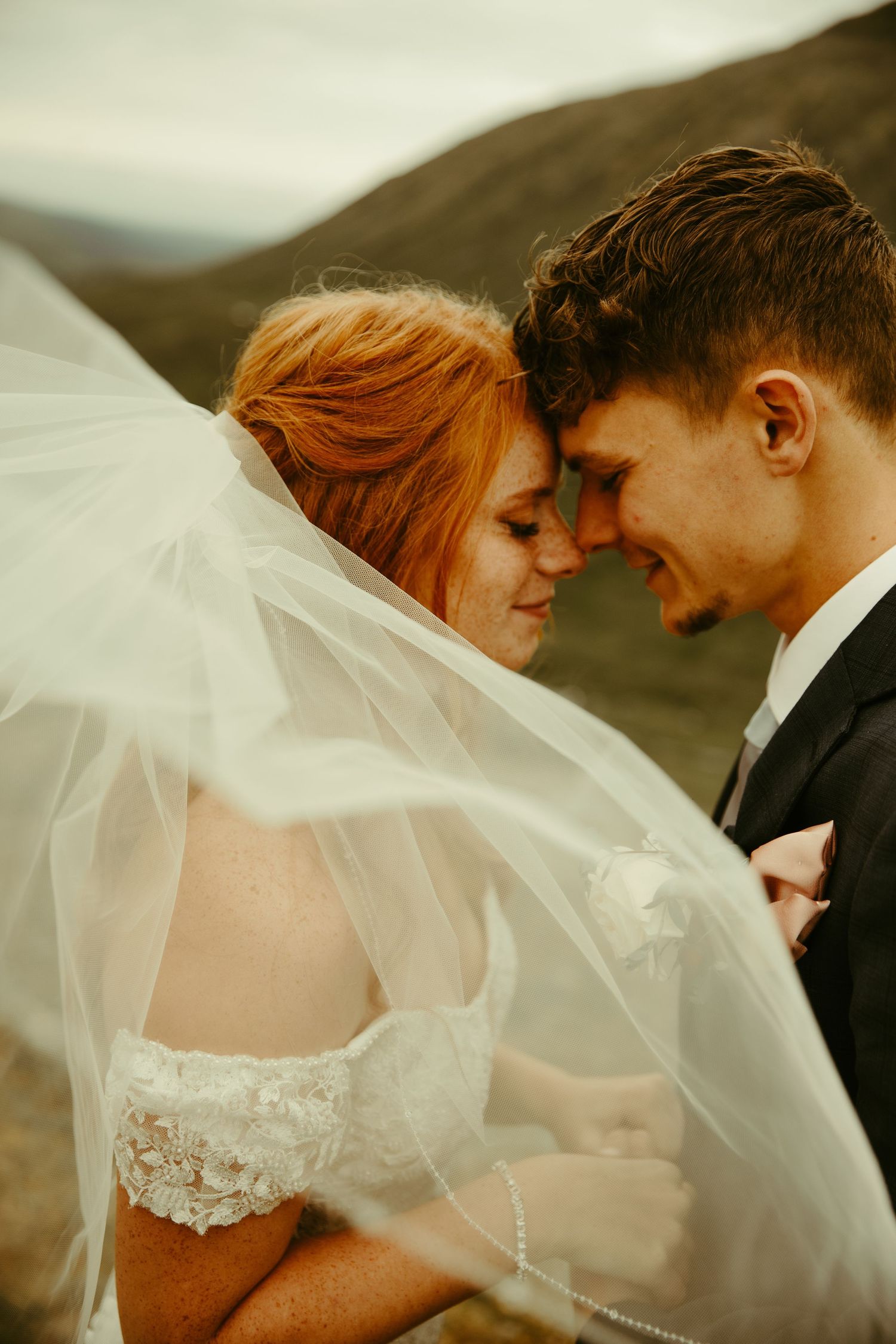 A romantic wedding photo shows a couple sharing an intimate moment as a delicate veil flows around them.