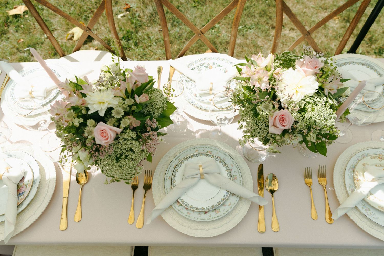 Elegant place settings with white plates, gold cutlery, and delicate floral centerpieces on a gray tablecloth at a formal event.