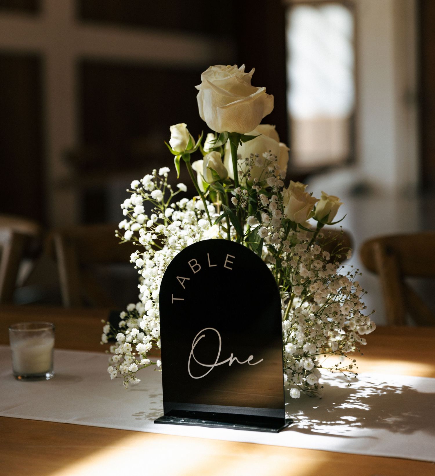 Elegant black table number with white roses and baby's breath floral arrangement for wedding reception decor.