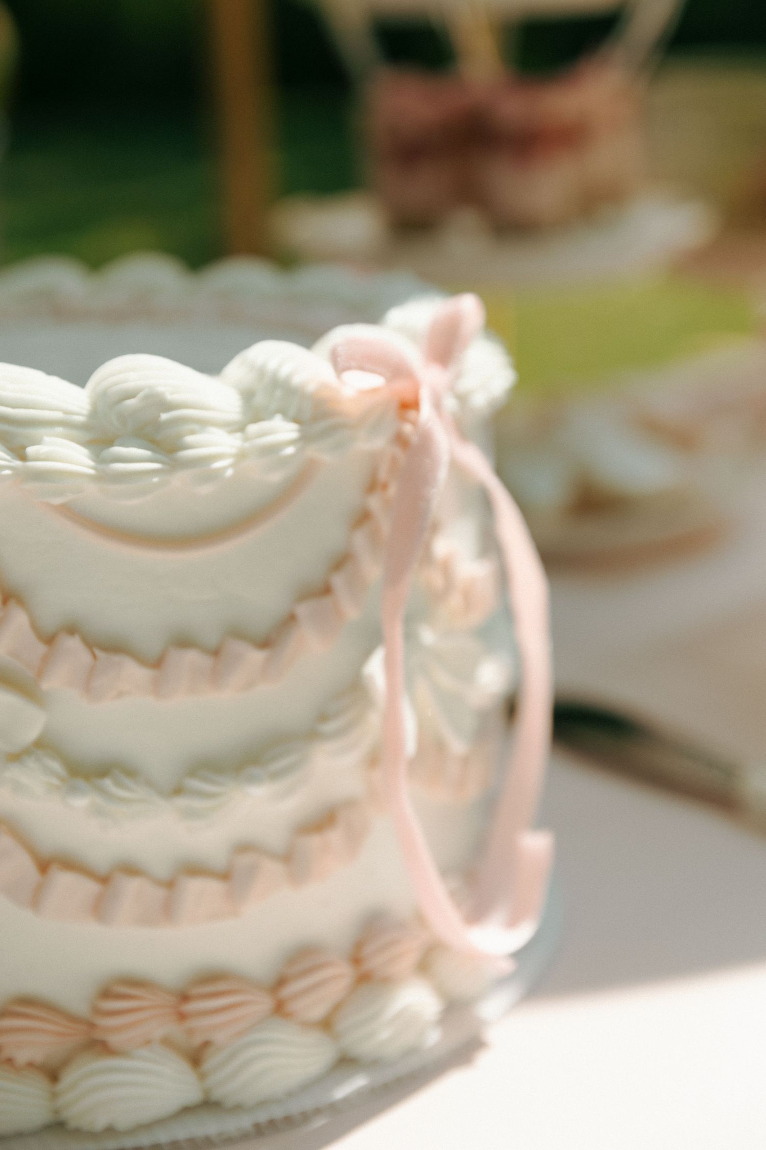 Close-up view of an elegant white wedding cake with delicate pink ribbon and piped frosting details.