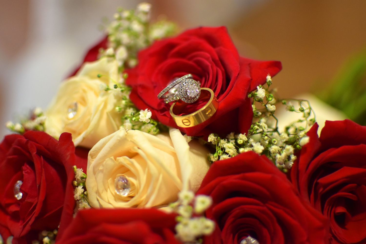 Wedding rings nestled among red and cream roses with baby's breath in an elegant bridal bouquet.