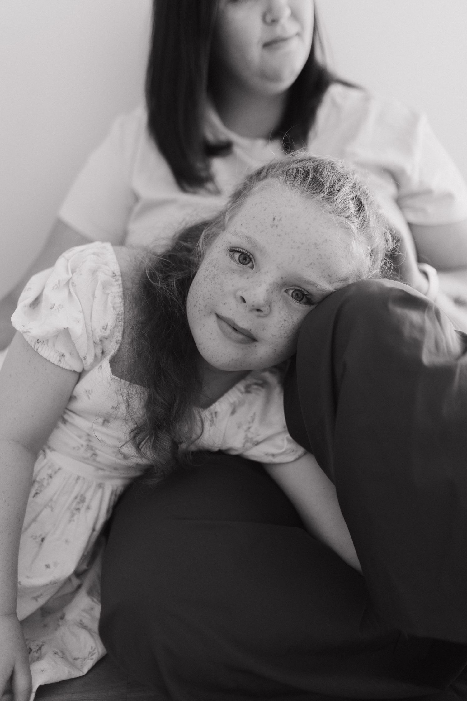Black and white photo of a freckled girl resting her head on her mother lap. At home photography.