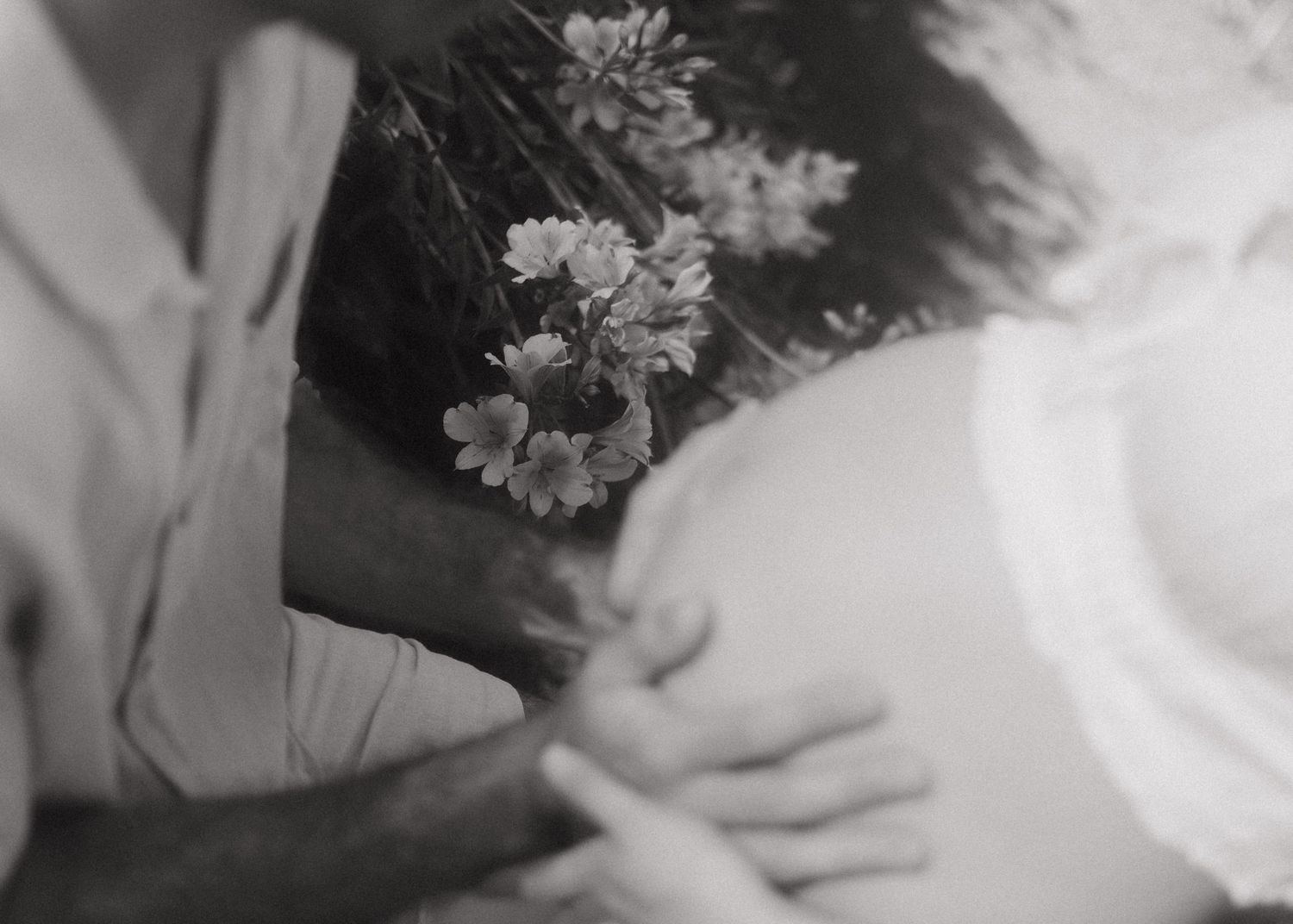 Black and white photo of a pregnant woman with flowers in her hair, cradling her baby bump tenderly.