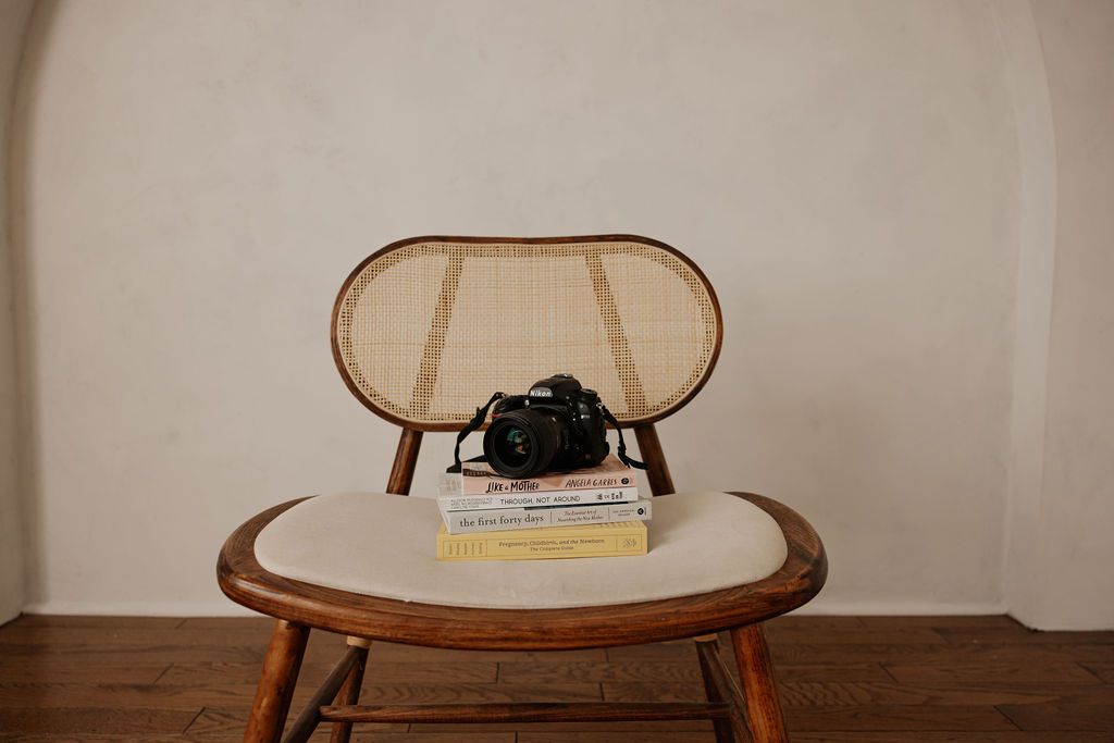 DSLR camera atop doula books on a chair Infront of a wall