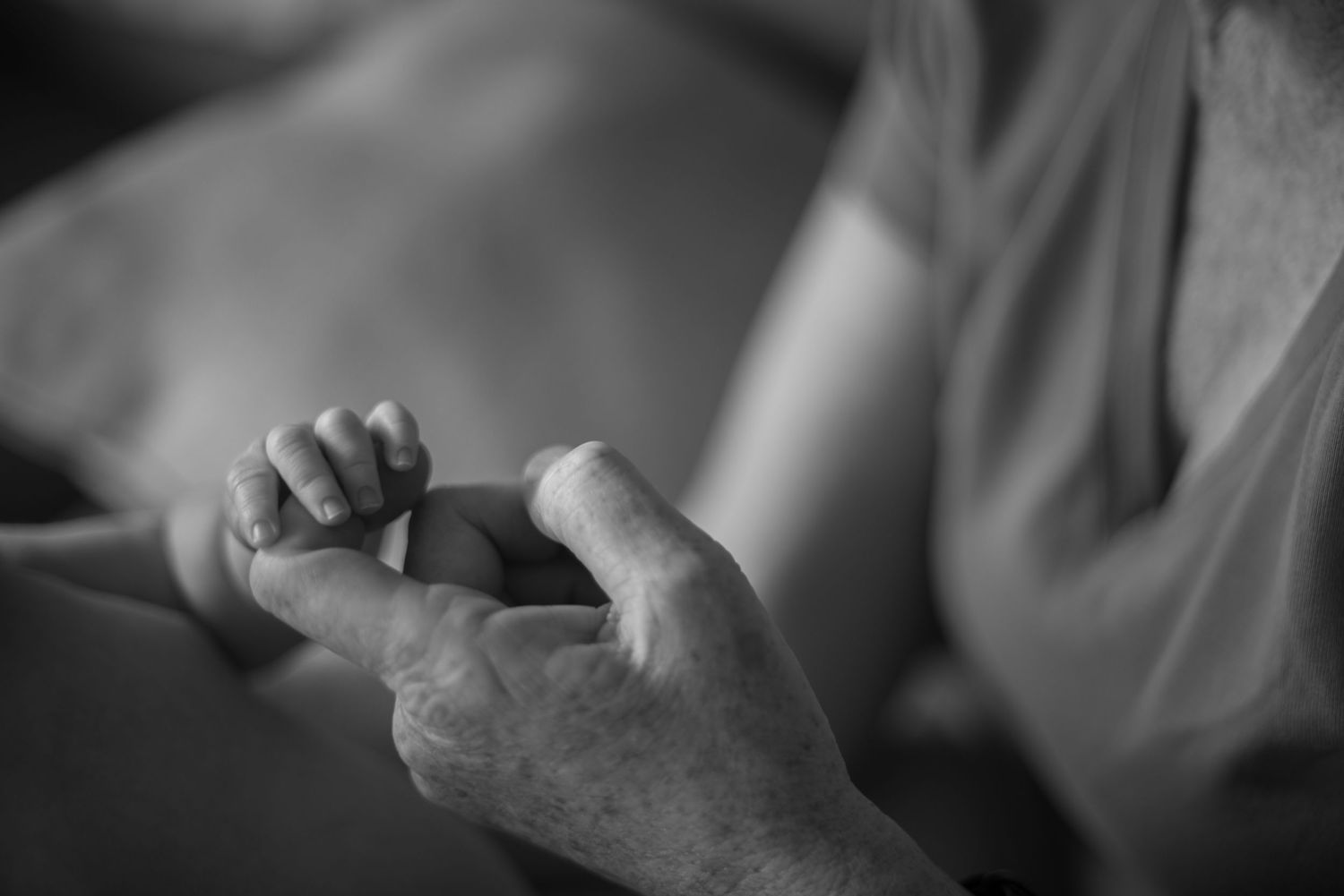a newborn grasping their grandparents hands for the first time