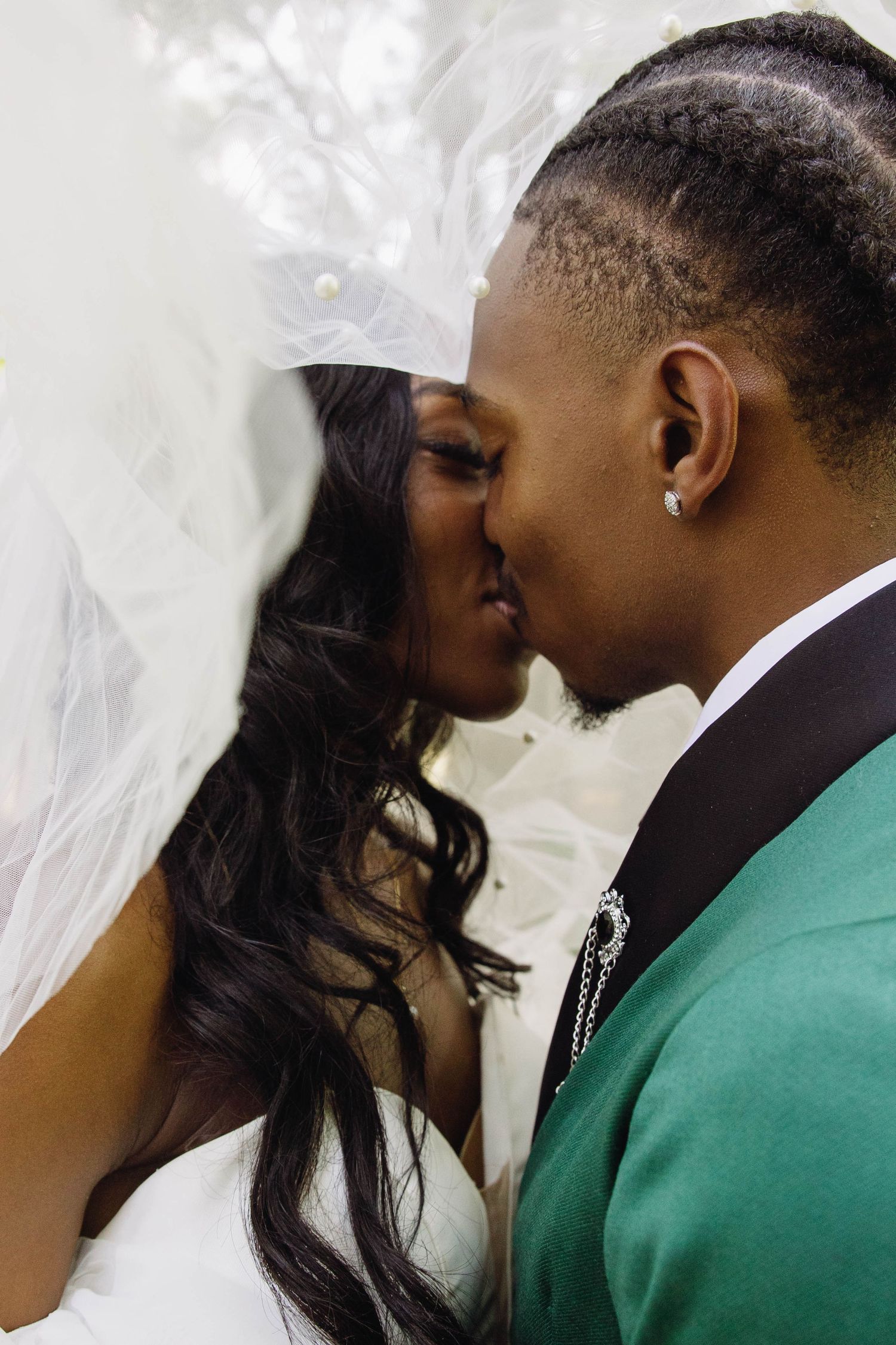 A couple in wedding attire share a romantic kiss, with the bride in white and groom in a green jacket.