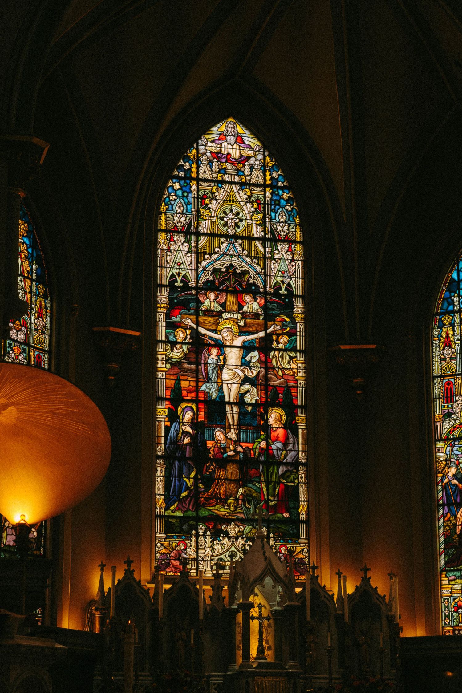 Gothic cathedral interior featuring a vibrant stained glass window depicting the crucifixion of Jesus Christ.