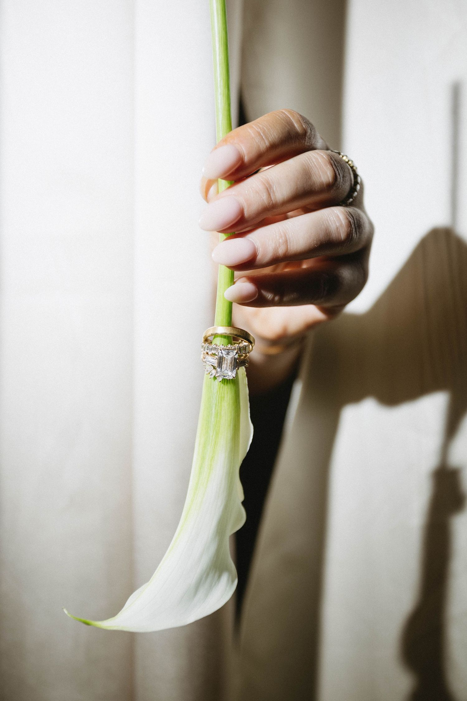 Hand holding a white calla lily with elegant diamond and gold wedding rings placed on the stem.