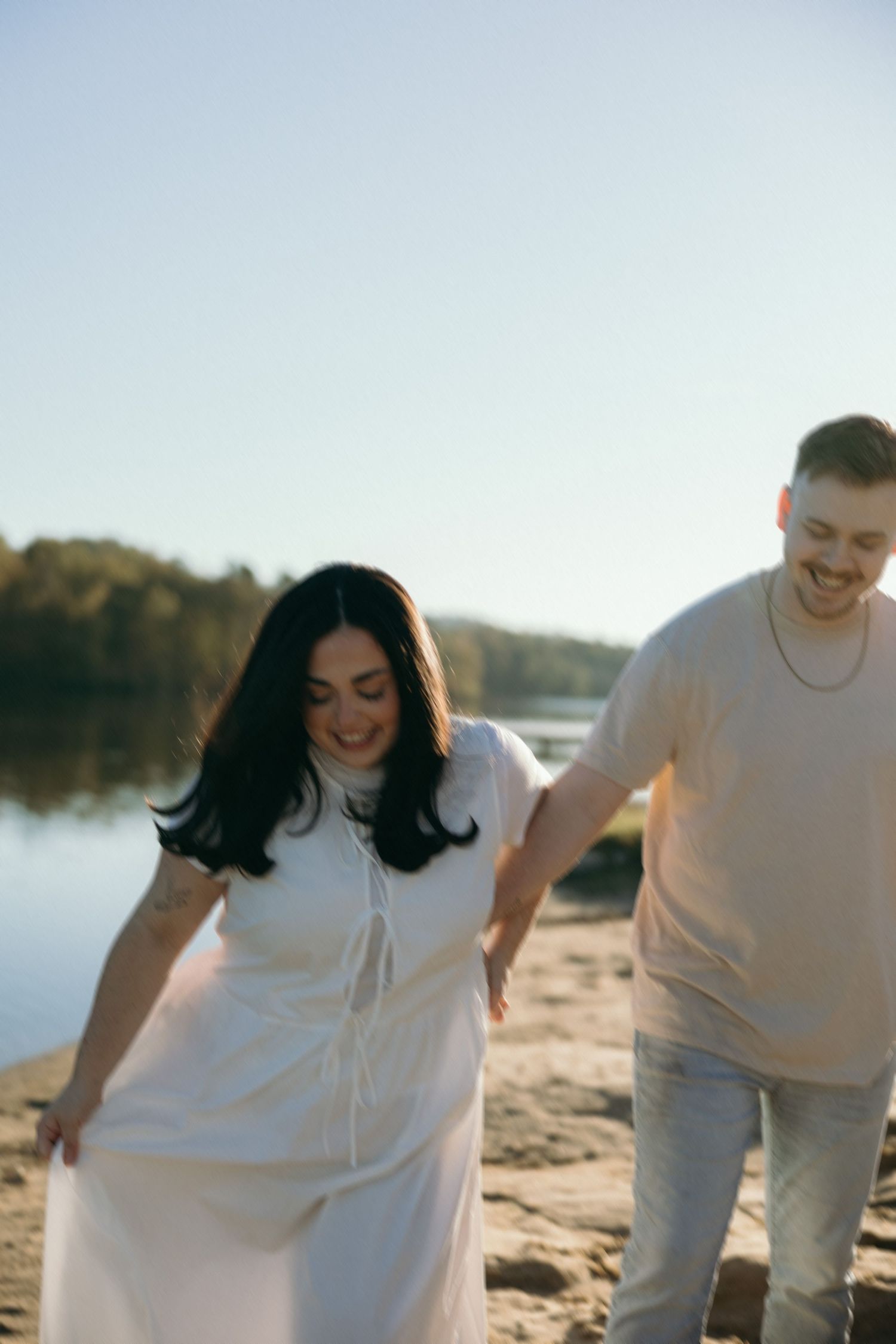 A couple walks along the shoreline at sunset, their joyful expressions lit by golden hour light.