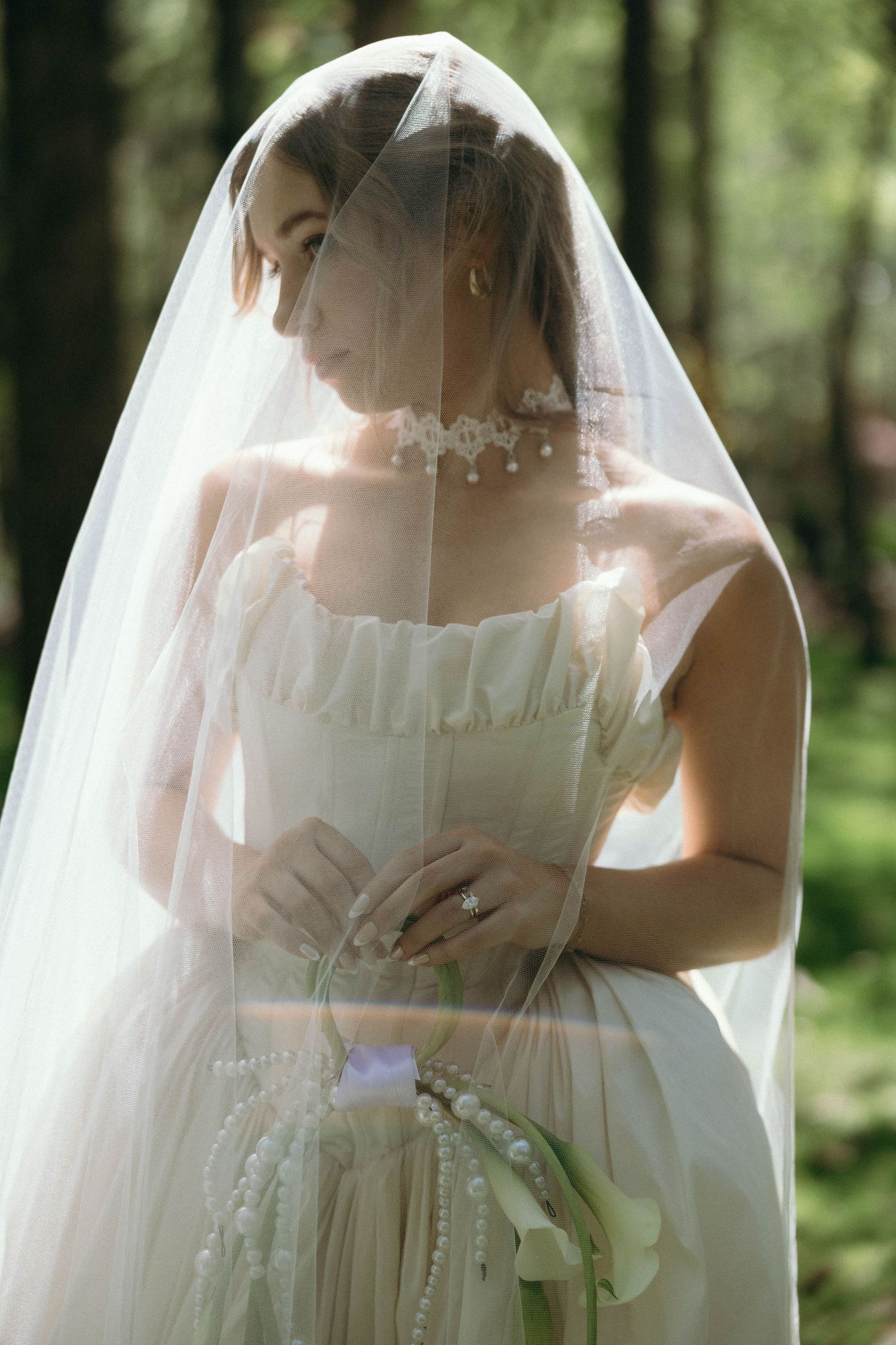 Ethereal bridal portrait in a forest setting shows a flowing white wedding dress and delicate veil in soft natural light.