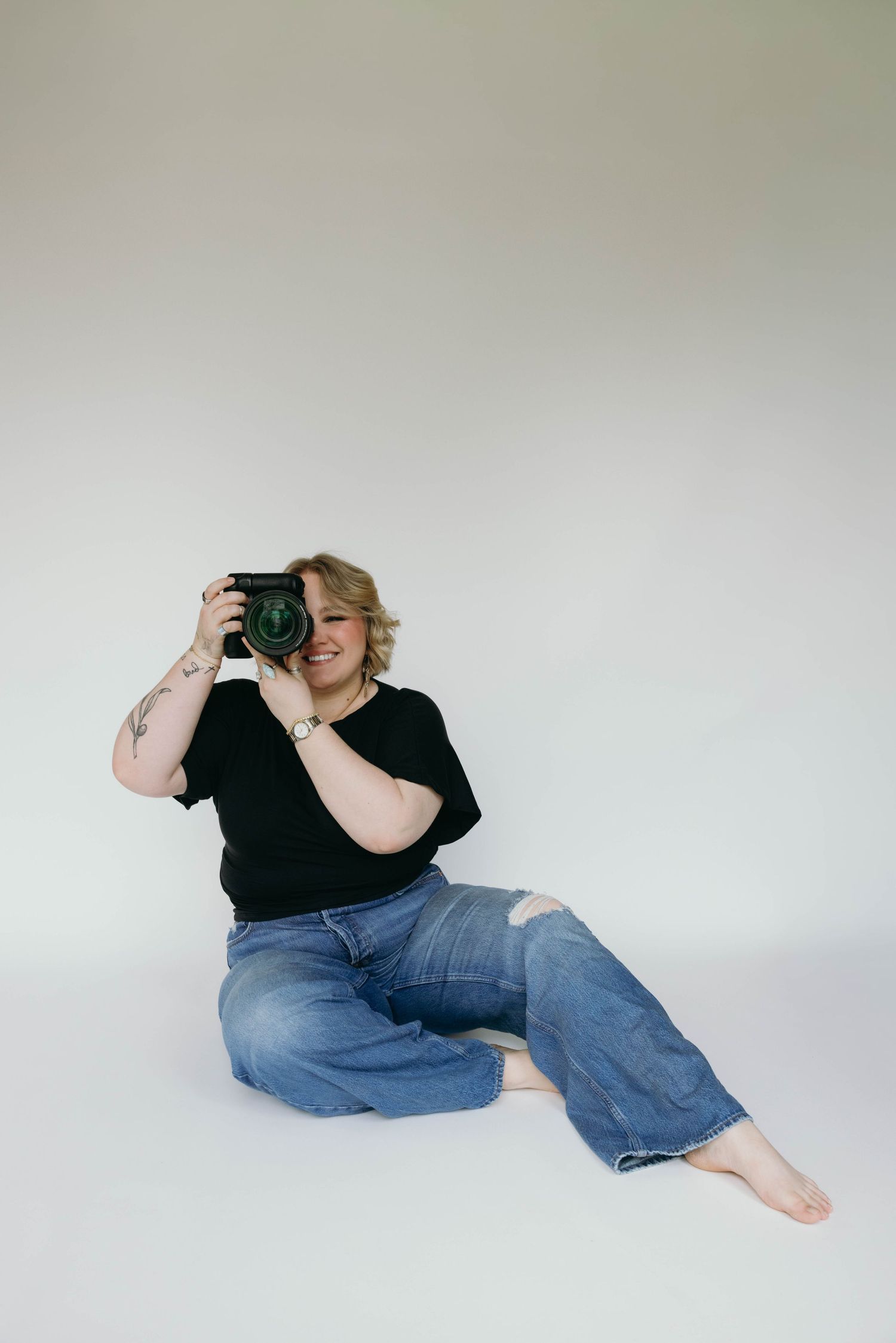 A photographer in black shirt and blue jeans lies on floor in various positions while taking photos against white background.