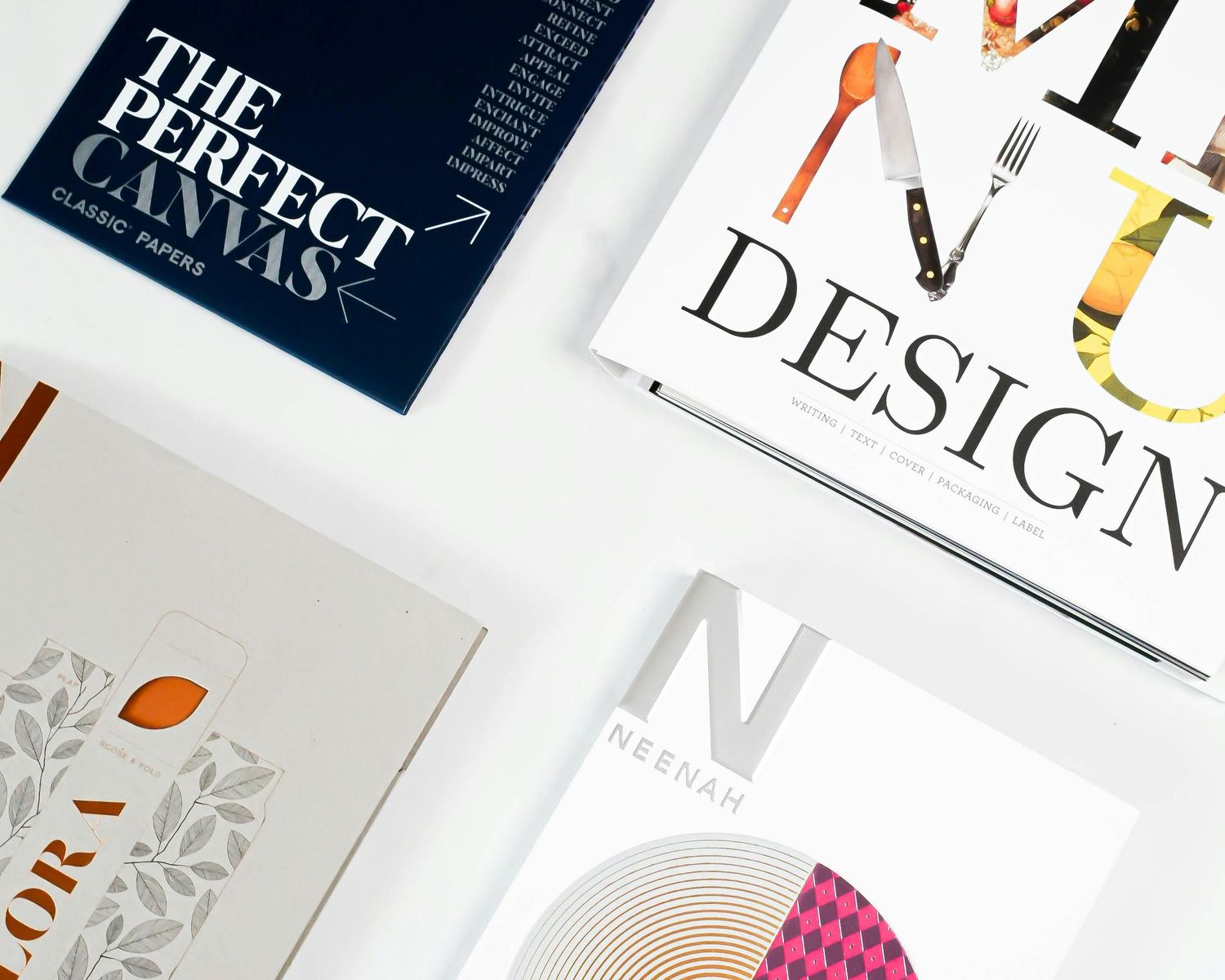 Four graphic design paper sample booklets arranged on white surface, including The Perfect Canvas and Neenah Design publications.