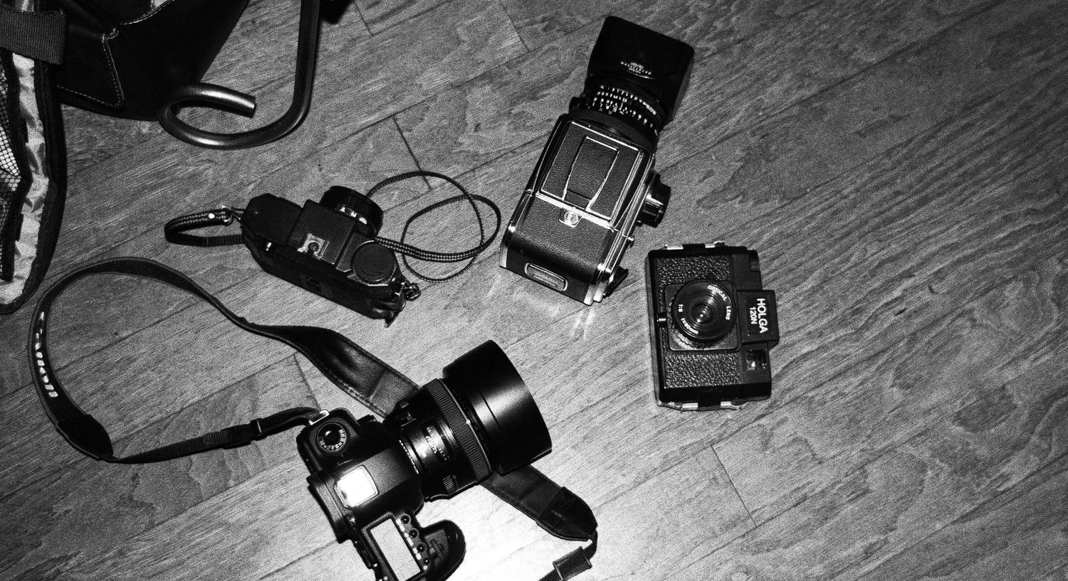 Black and white flat lay of vintage cameras and photography equipment on a wooden floor.