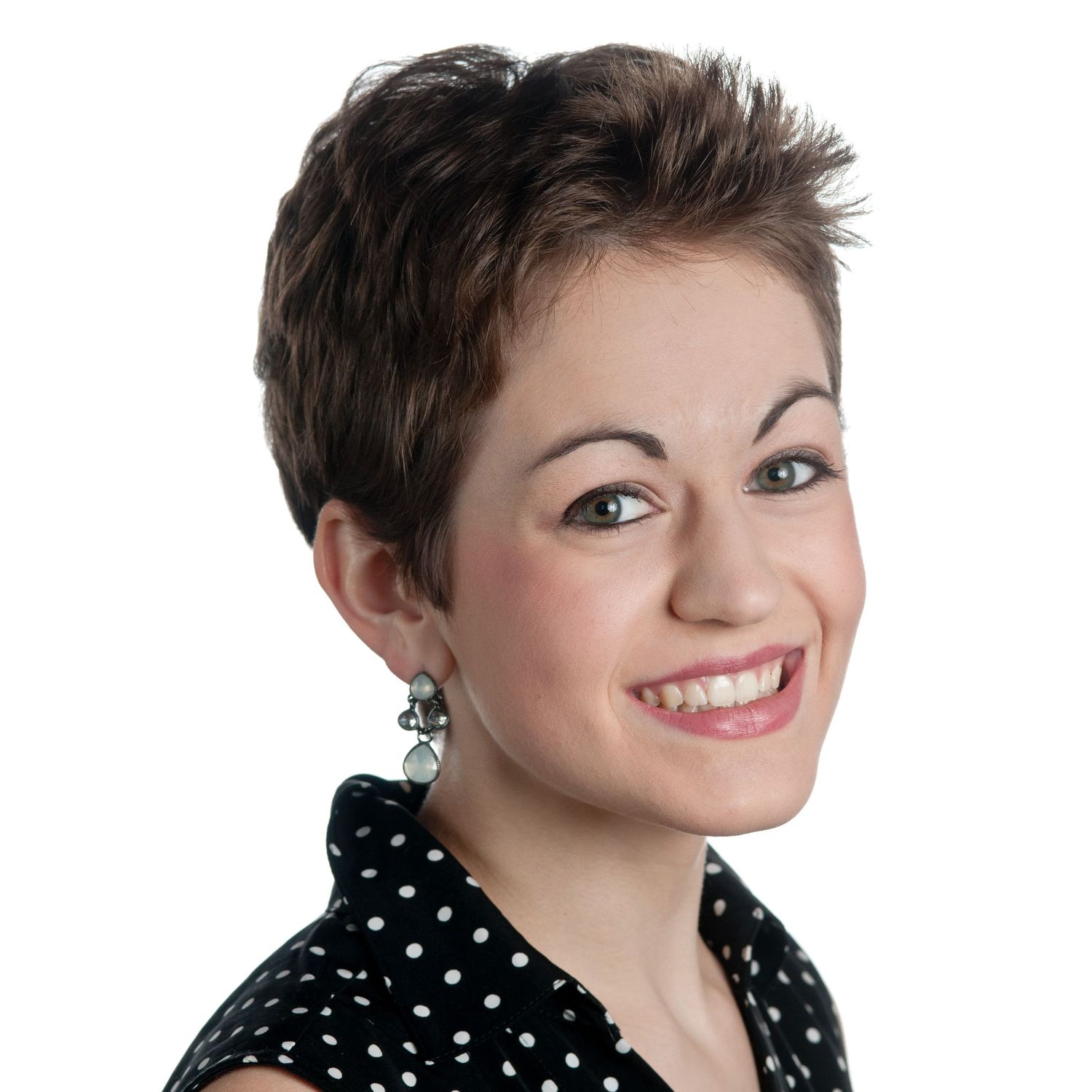 Professional headshot of a smiling woman with short dark hair wearing a black polka dot top and decorative earrings.