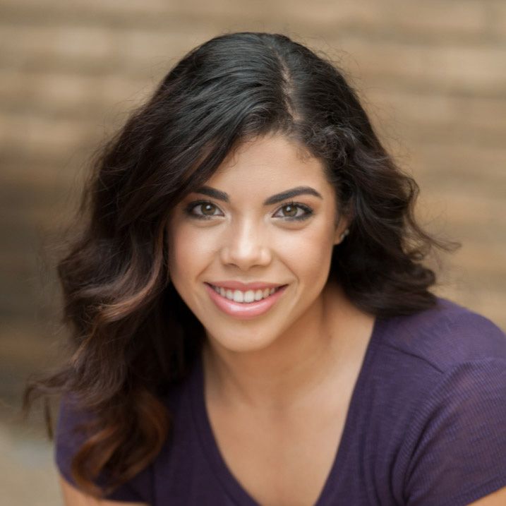 Smiling woman with wavy dark hair wearing a purple top in an outdoor portrait headshot.