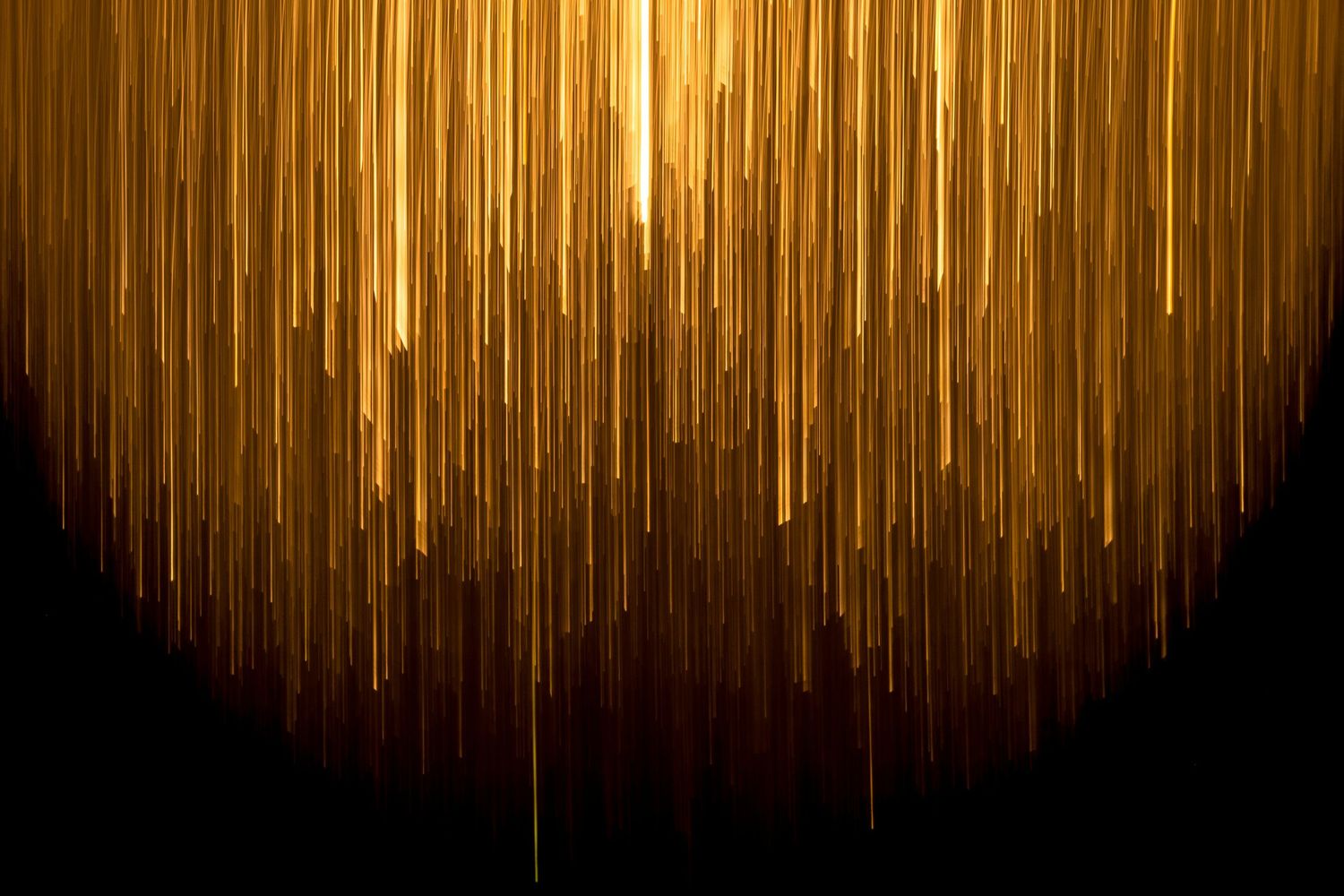 Golden rain streaks cascade down a dark background creating an elegant abstract light effect.