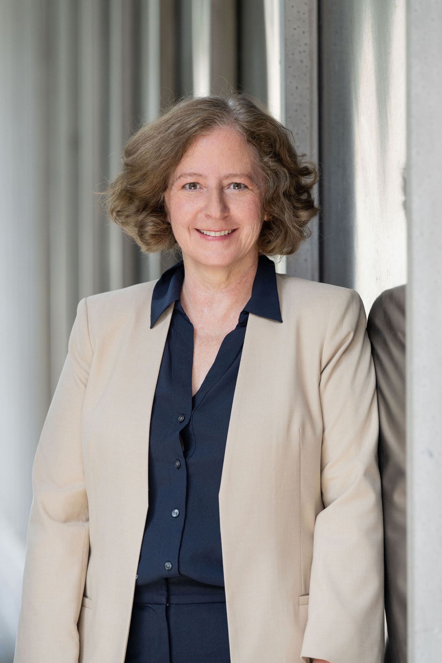 Professional woman in a beige blazer smiling for a corporate headshot outdoors.