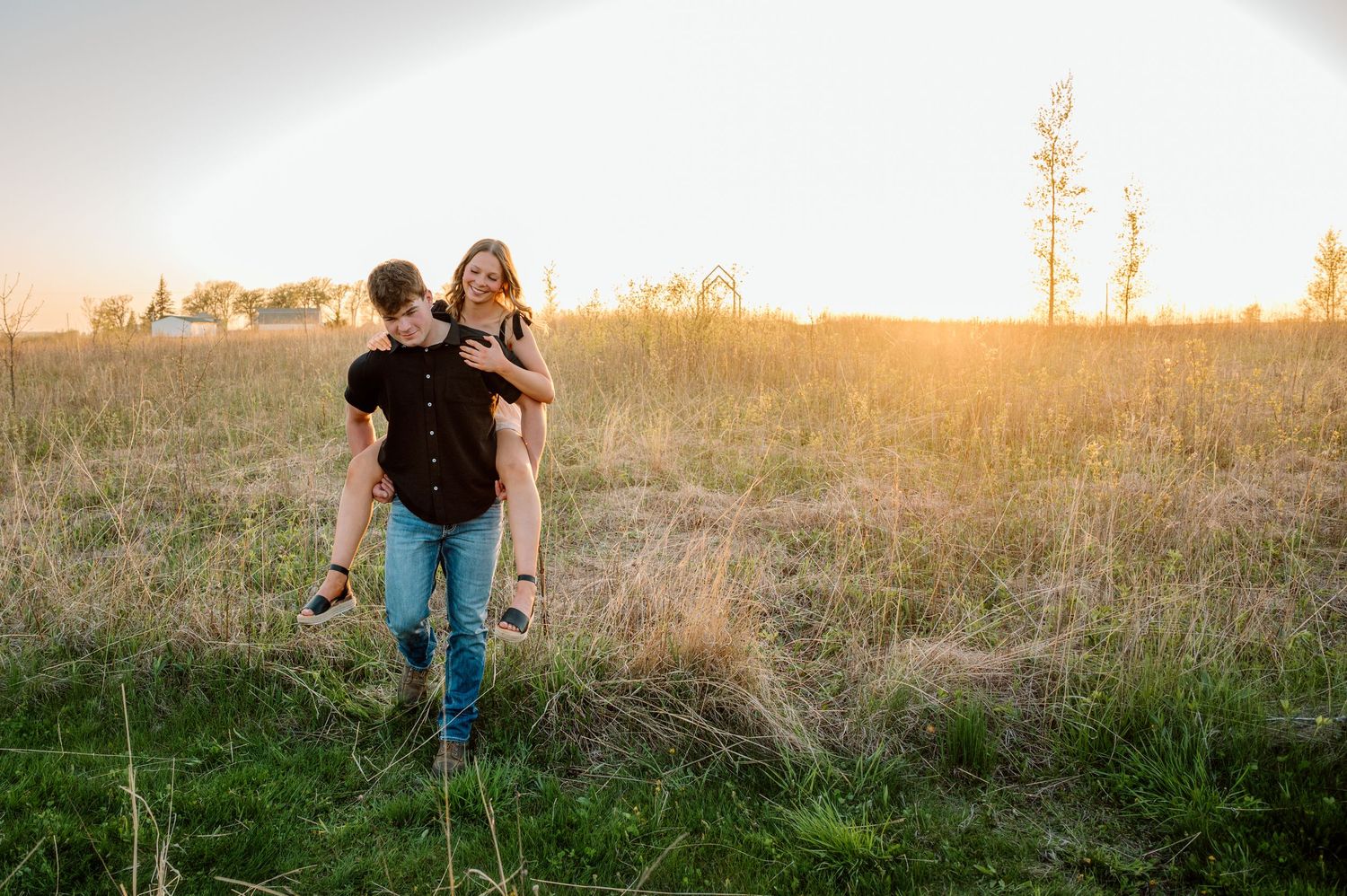 A playful couple shares a piggyback ride in a golden sunlit meadow during sunset.