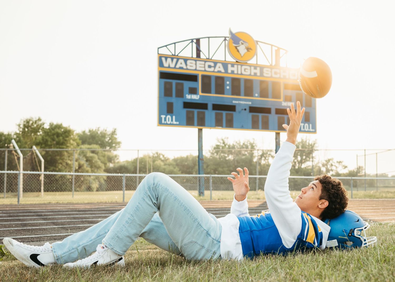 Student athlete lying on grass field in front of scoreboard at sunset.
