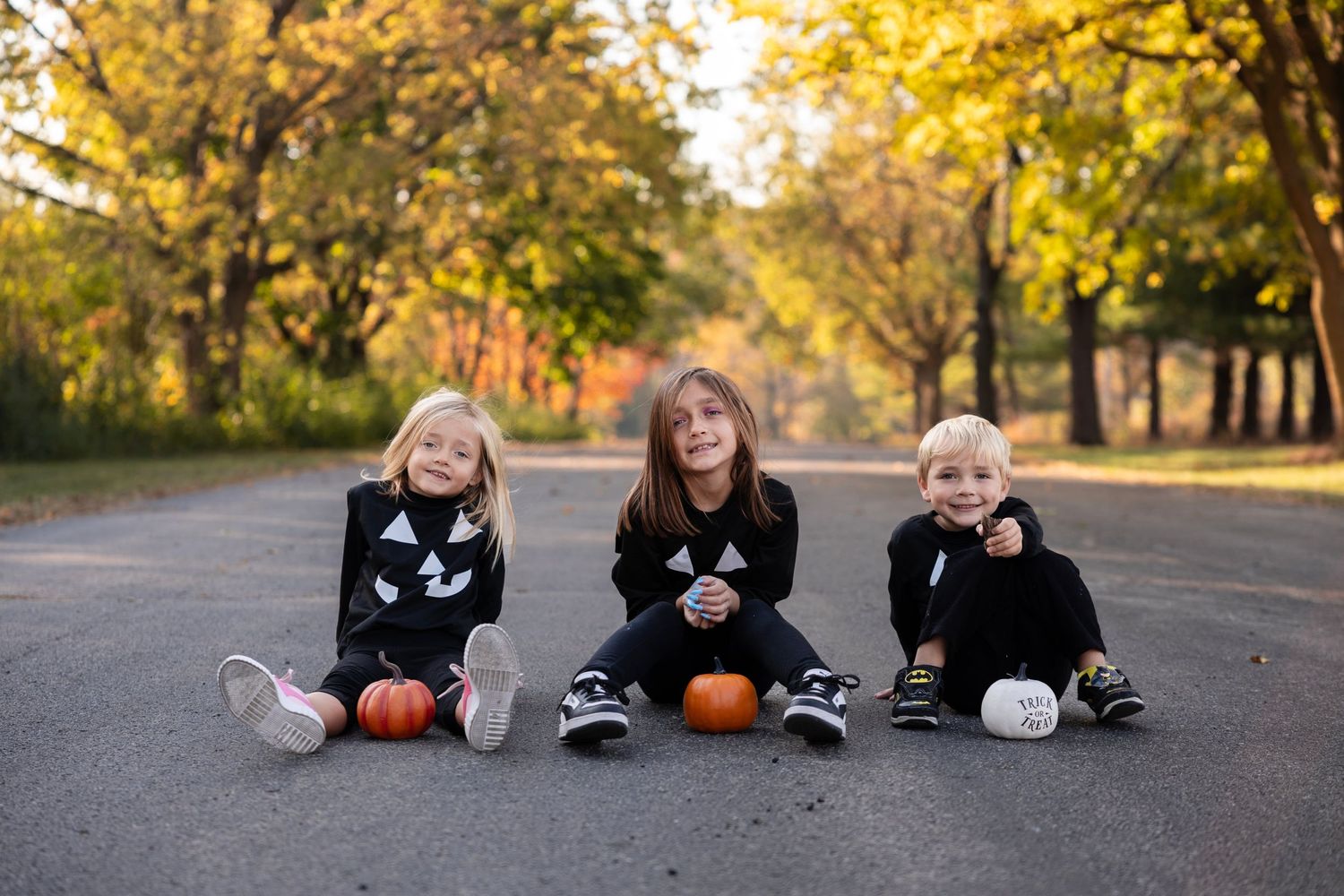 Halloween and fall-themed photoshoot featuring young siblings in festive shirts, surrounded by pumpkins and autumn leave