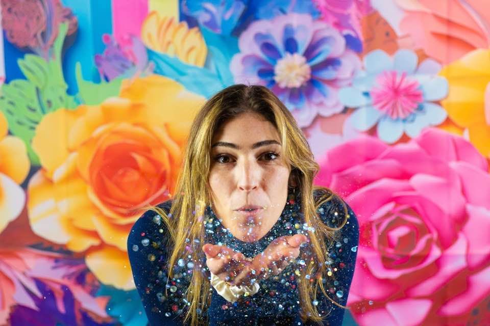 A vibrant branding photo of a business owner playfully blowing glitter, set against a fun, festive background filled wit