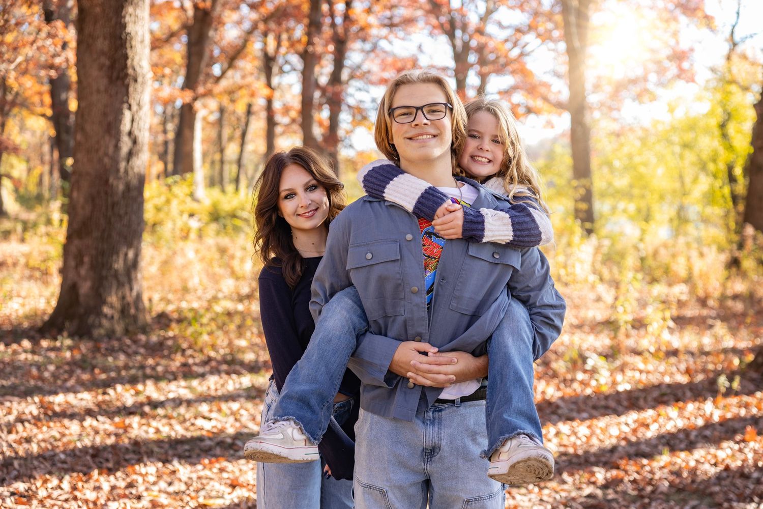 Fun sibling photo captured during golden hour in Elgin, IL, featuring a girl playfully on her big brother's back and ano