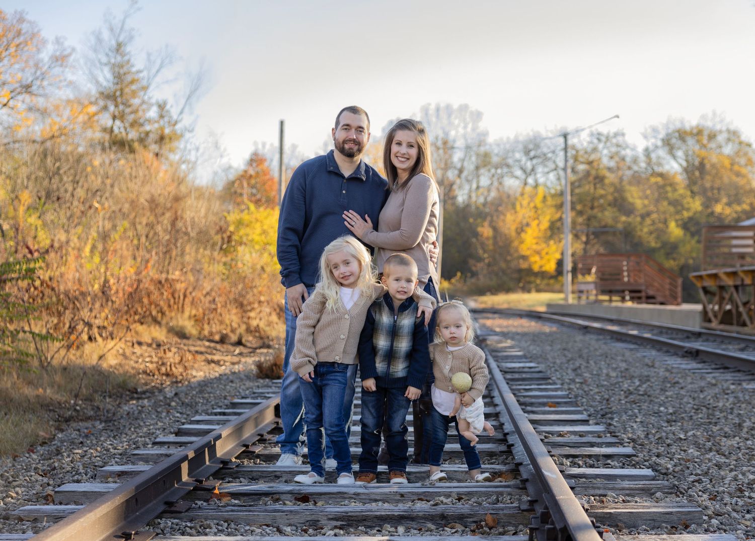 A touching photoshoot of a small, growing family standing together on rustic train tracks, symbolizing their journey ahe